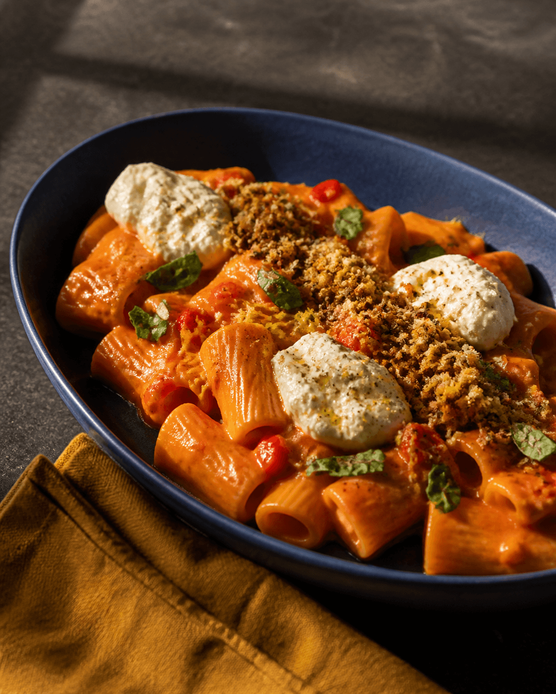 Rigatoni i blank murstensrød vodkatomatsauce med ristede pebertern, citron, tre ricottaqueneller og brødkrumme på dyb koboltblå oval skål