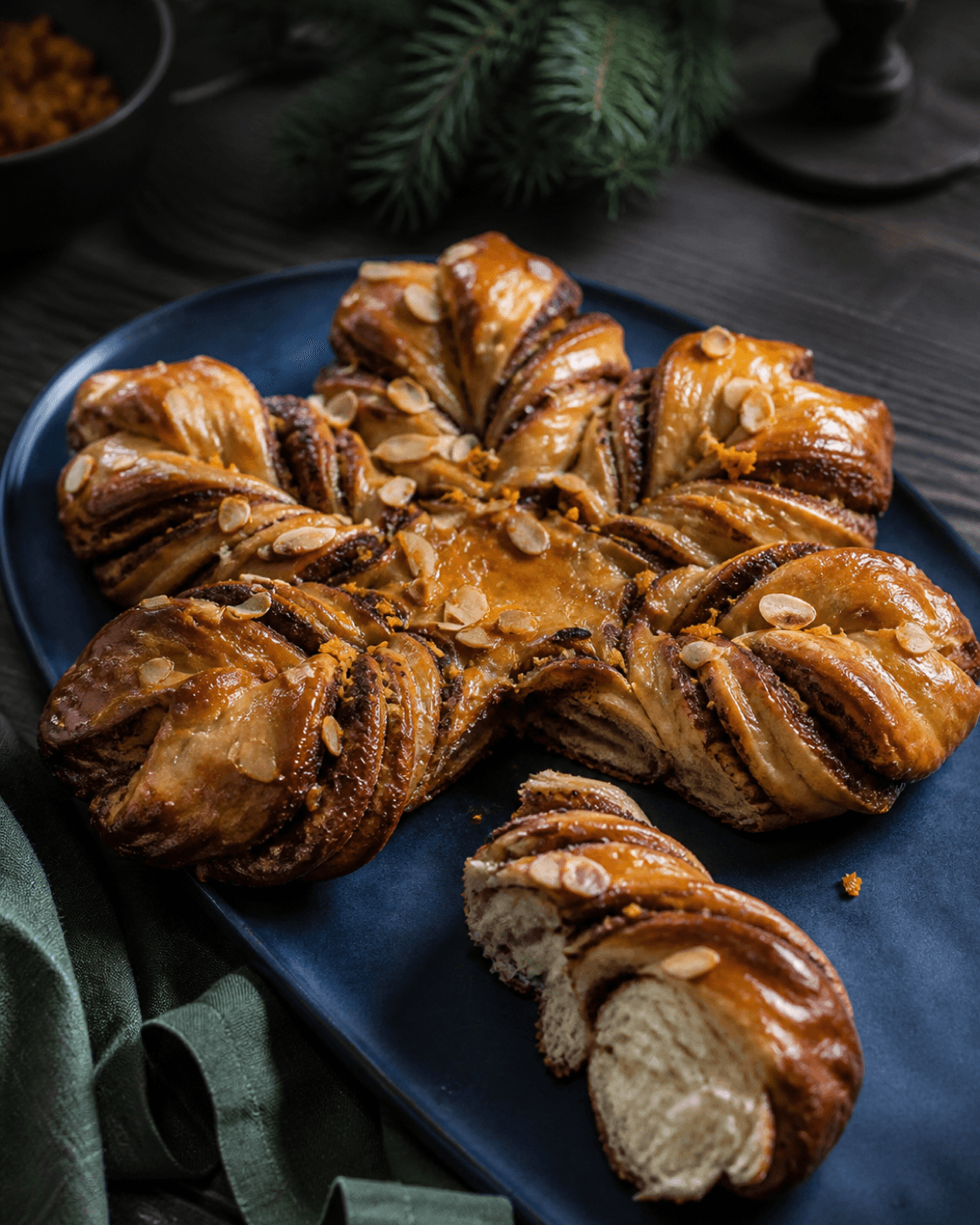 Dybt gylden ottepunktet kanelstjerne med appelsin, mandel og synlige lag på mat koboltblåt fad, ét punkt revet åbent