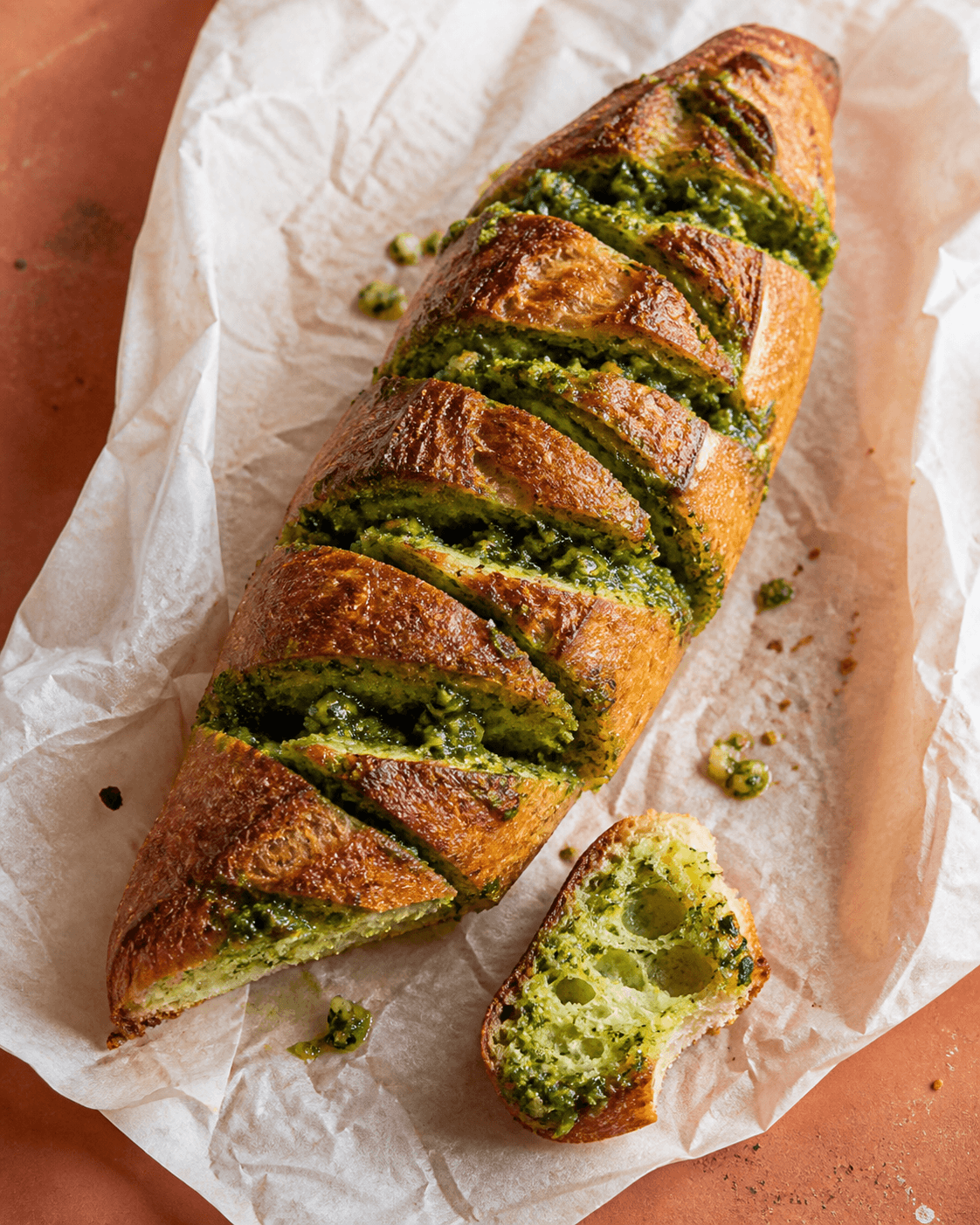 Gyldent hvidløgsbrød med dybe snit, grønt persillesmør og åben saftig krumme på terracotta
