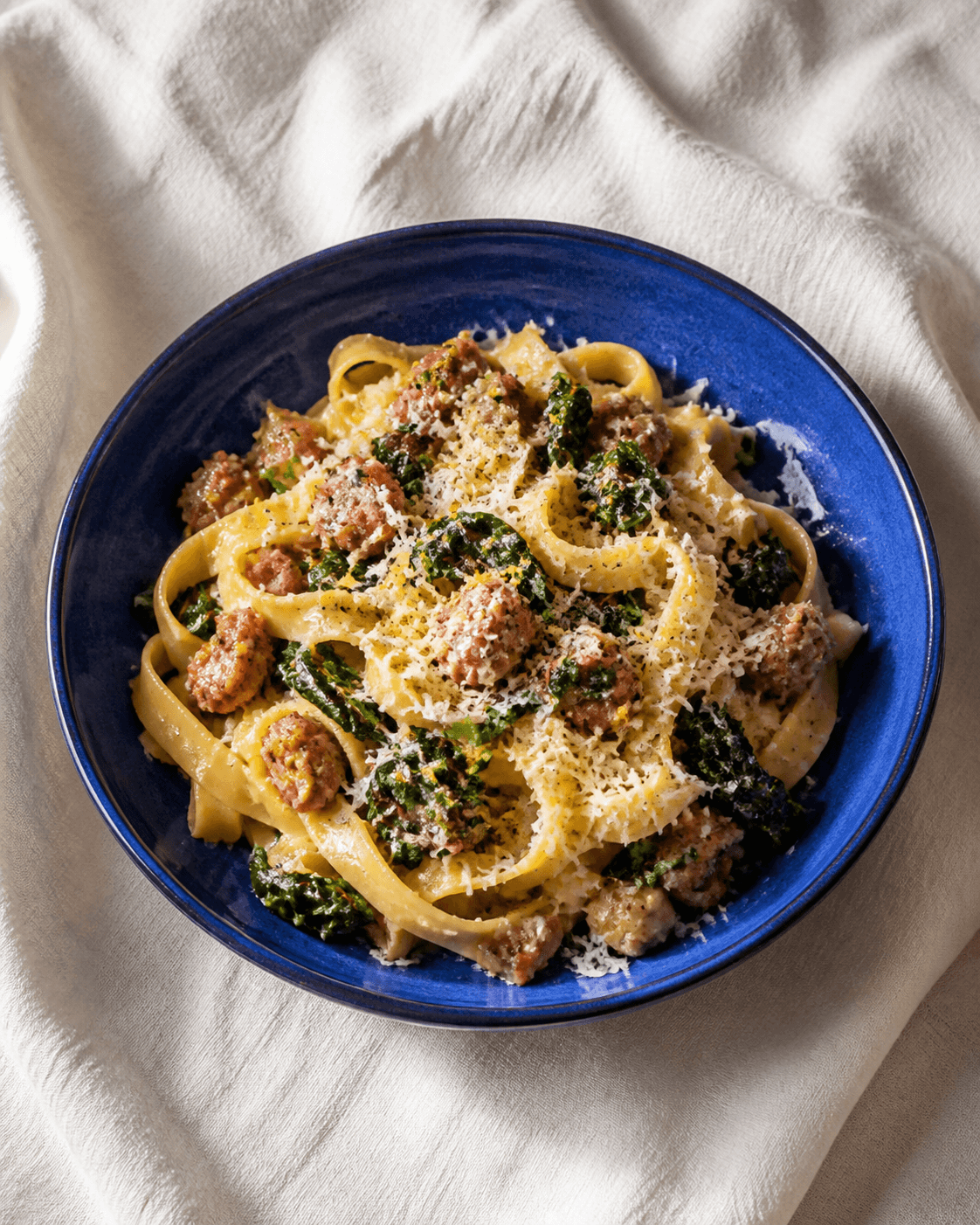 Blank tagliatelle med salsiccia, mørk cavolo nero, citron og ost i koboltblå skål