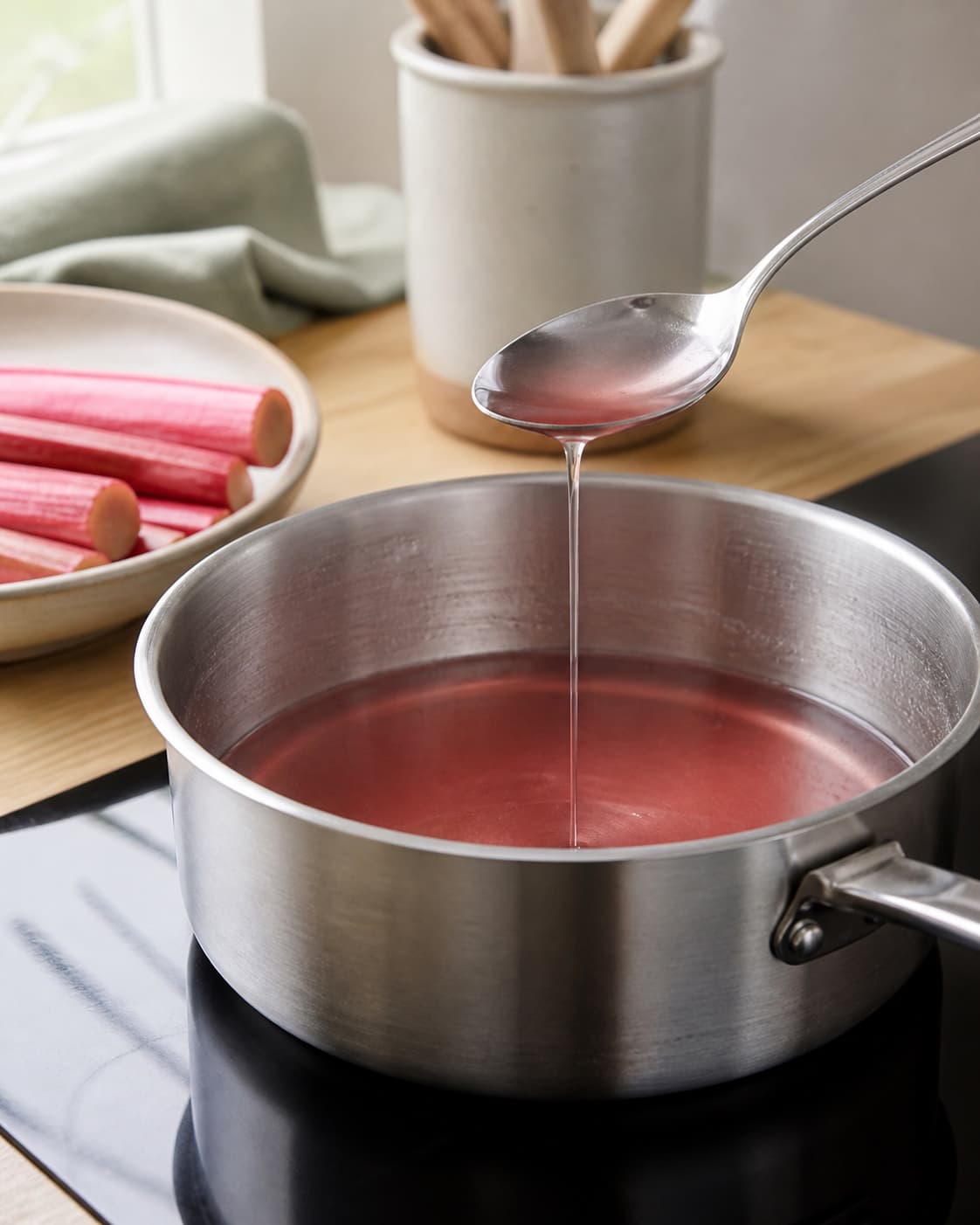 blank klar rosarød rabarbersirup falder langsomt fra en ren ske i bred gryde ved siden af et digitalt termometer; kontroltegnet er siruppen er blank og klar rosa med en langsom sammenhængende stråle uden skum