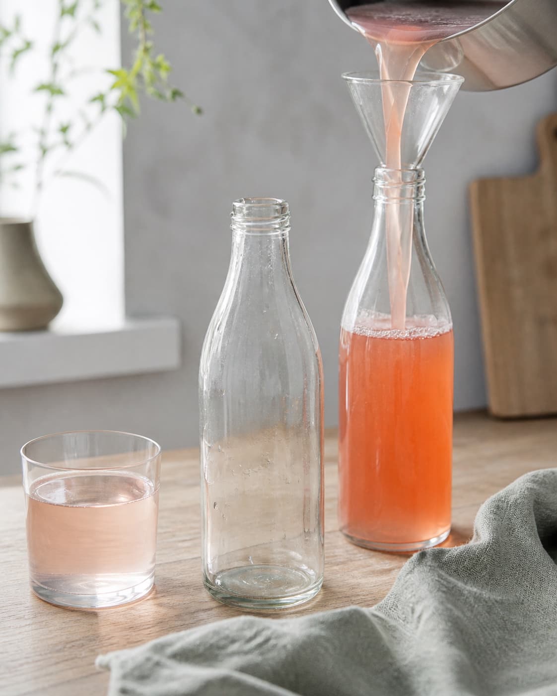 varm klar rabarbersaft fyldes gennem ren tragt i udekorerede flasker ved siden af et meget lyst rosa fortyndet glas; kontroltegnet er flaskerne er rene og hurtigt kolde, mens en fortyndet prøve er klar meget lys rosa