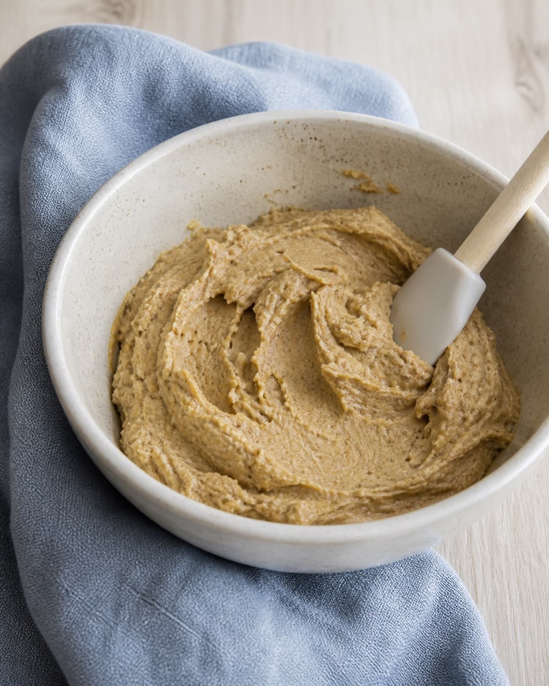tyk gylden cookie-dej er netop foldet sammen i stentøjsskål med enkelte næsten forsvundne melstriber; kontroltegnet er dejen er tyk, blank-mat og netop samlet uden tørt mel eller luftig overpiskning