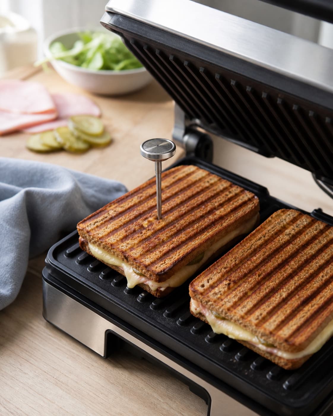 to lukkede toast grilles med mørkgyldne parallelle riller og lidt synlig smeltet ost mens et rent termometer sidder i centrum af én toast; kontroltegnet er brødet har mørkgyldne sprøde riller, osten er helt smeltet, og centrum måler mindst 75 °c