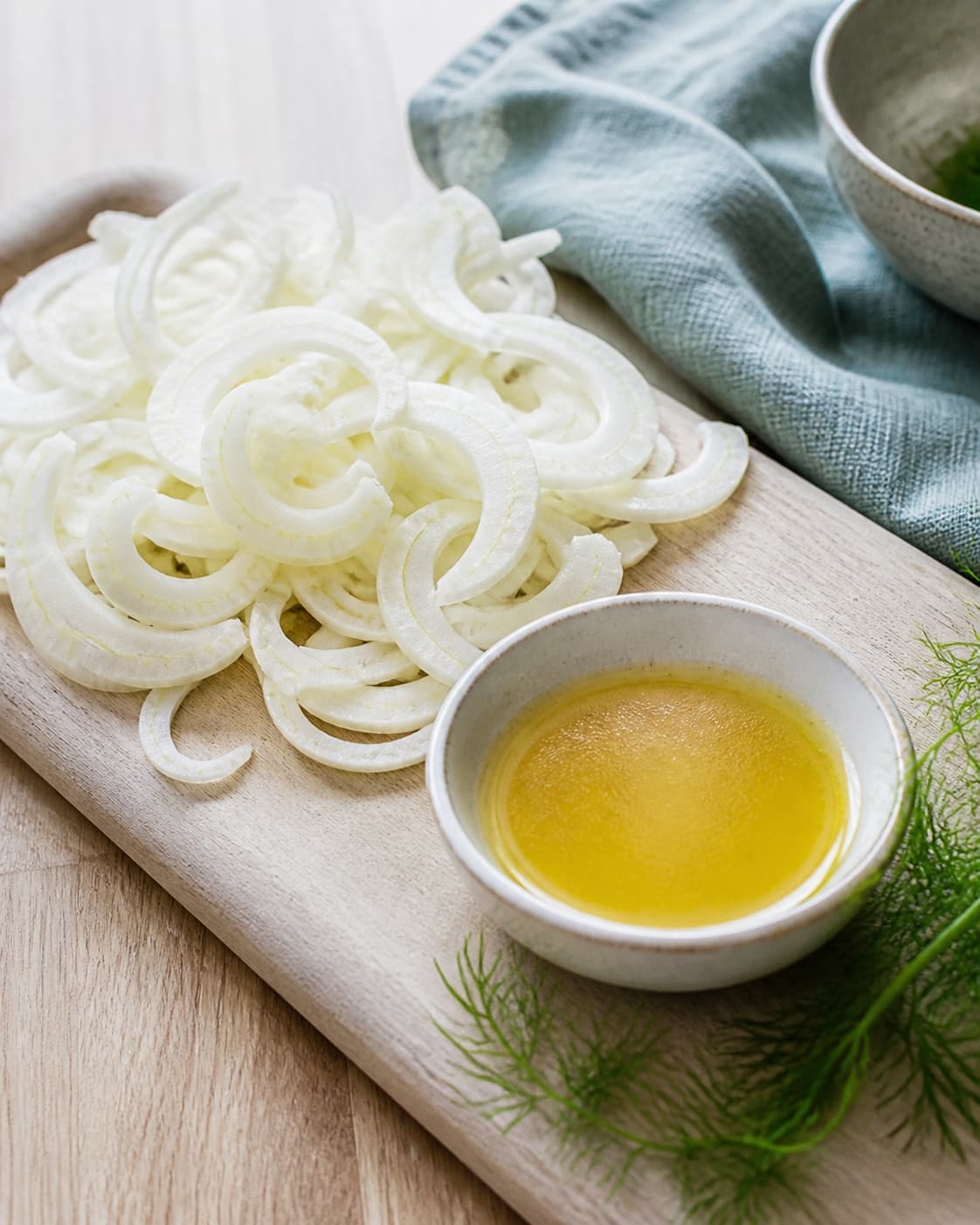 papirtynde hvide fennikelbuer ligger helt tørre og sprøde ved siden af en lille skål blank gylden citrusdressing og nogle grønne fennikeltoppe; kontroltegnet er fenniklen er papirtynd, buet og sprød uden vanddråber, og dressingen er blank og let emulgeret uden uopløst honning