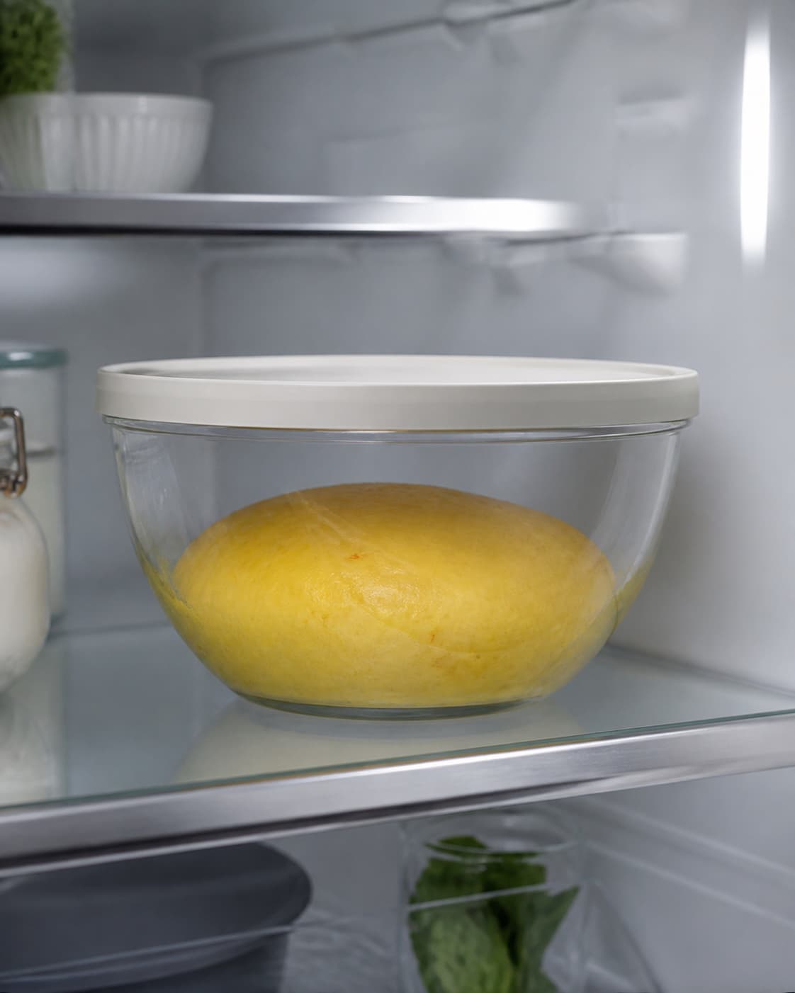 koldhævet dybgul dej med glat hvælvet overflade og tydelig moderat volumenstigning ligger i en ren dækket glasskål på en kølig hylde; kontroltegnet er dejen er efter kulden vokset omtrent 60–80 procent, har en glat hvælvet overflade og dufter mildt gæret uden sprit- eller rådden tone