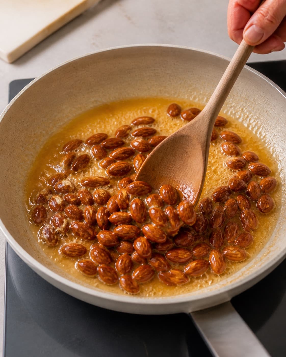 Whole almonds being coated in a light amber butter caramel in a wide pan under tilberedningen af appelsinsauce og karameliserede mandler til risalamande