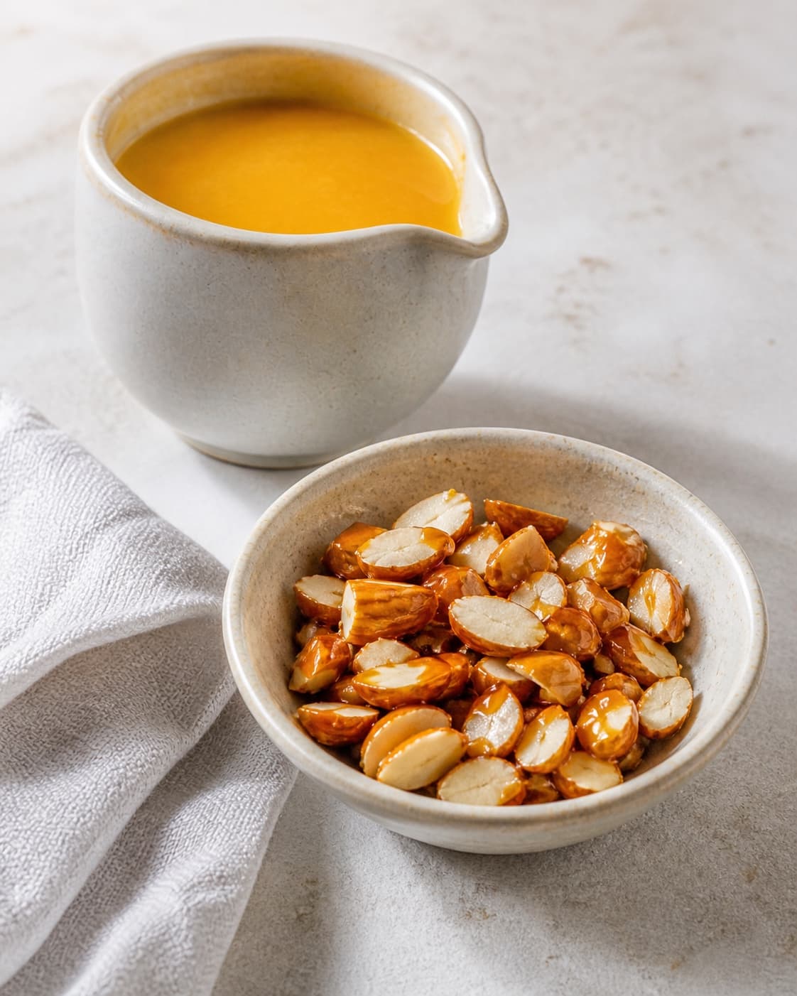 Warm orange sauce in a jug beside chopped crisp caramelised almonds for risalamande under tilberedningen af appelsinsauce og karameliserede mandler til risalamande