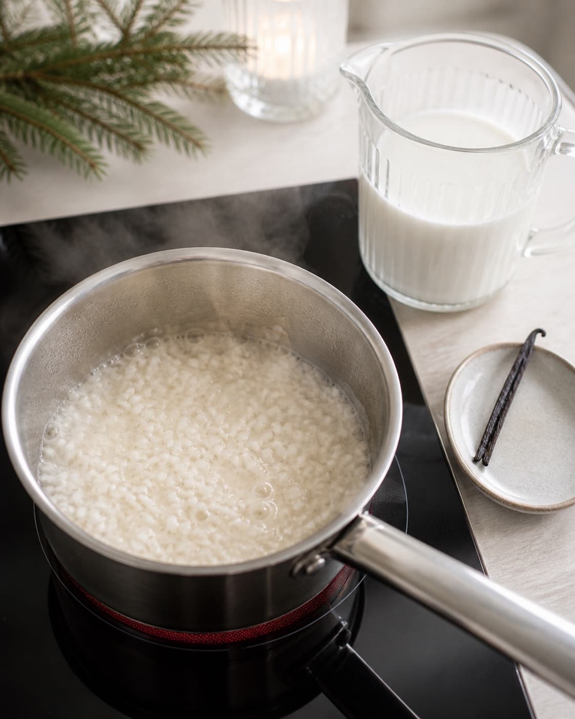 Porridge rice simmering briefly in water beside a split vanilla bean and measured milk under tilberedningen af risalamande