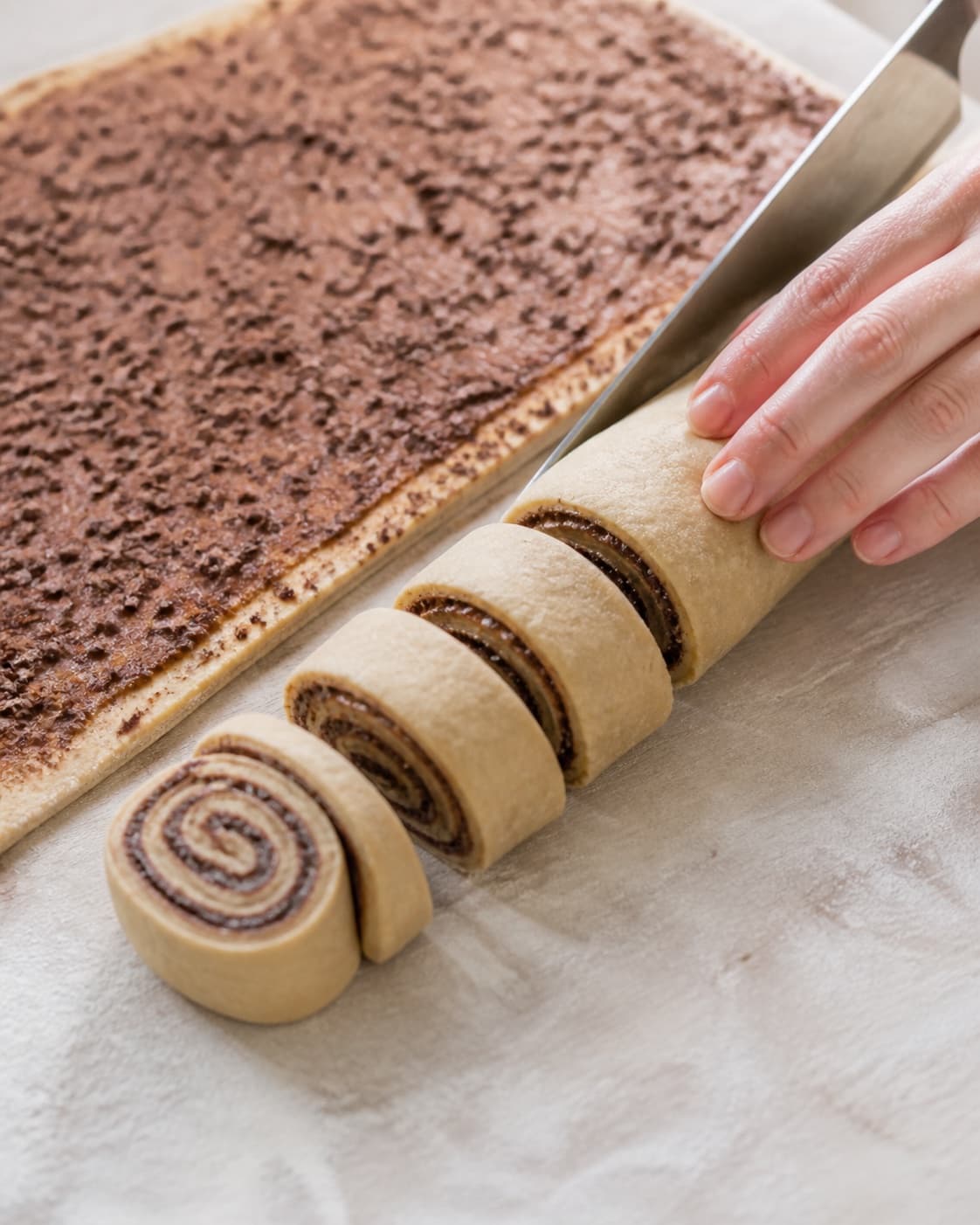 Cinnamon chocolate filled dough roll being cut into equal spiral buns under tilberedningen af kanelboller med chokolade