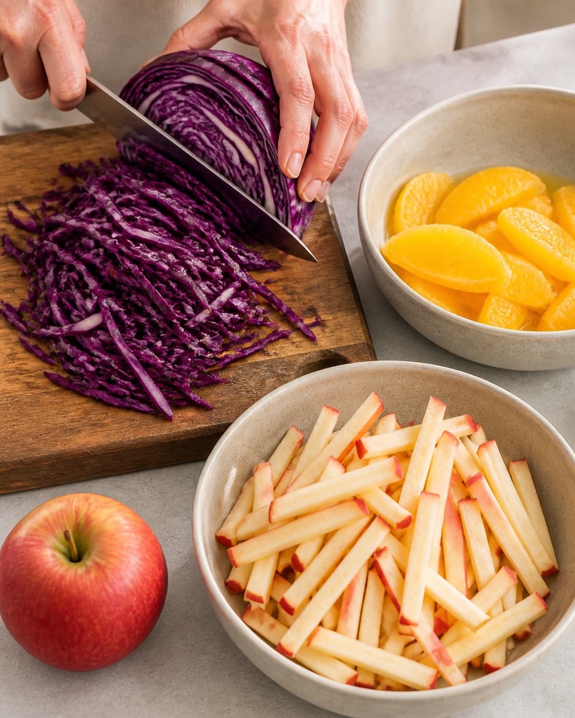 Red cabbage finely sliced while apples and orange supremes are cut evenly under tilberedningen af rødkålssalat med æble