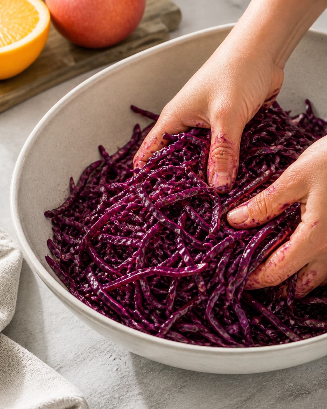 Fine red cabbage being massaged with dressing before apple and orange are folded in under tilberedningen af rødkålssalat med æble