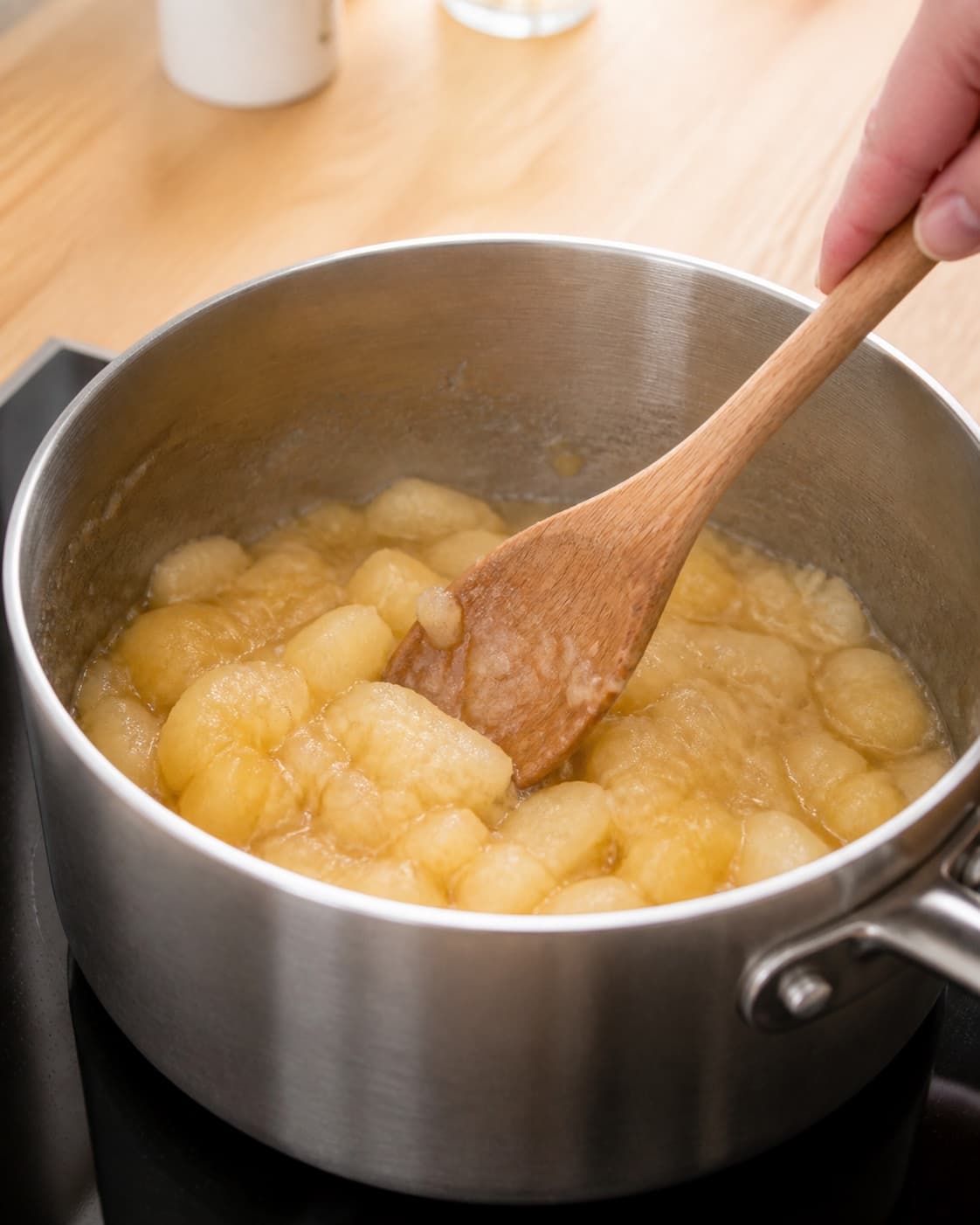 Tart apple pieces simmering with sugar vanilla and a little water into a textured compote under tilberedningen af gammeldags æblekage med ristet rasp og flødeskum