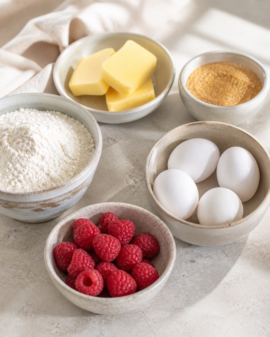 Muffin tin beside dry raspberries and measured flour baking powder vanilla salt butter sugar eggs and milk under tilberedningen af hindbærmuffins