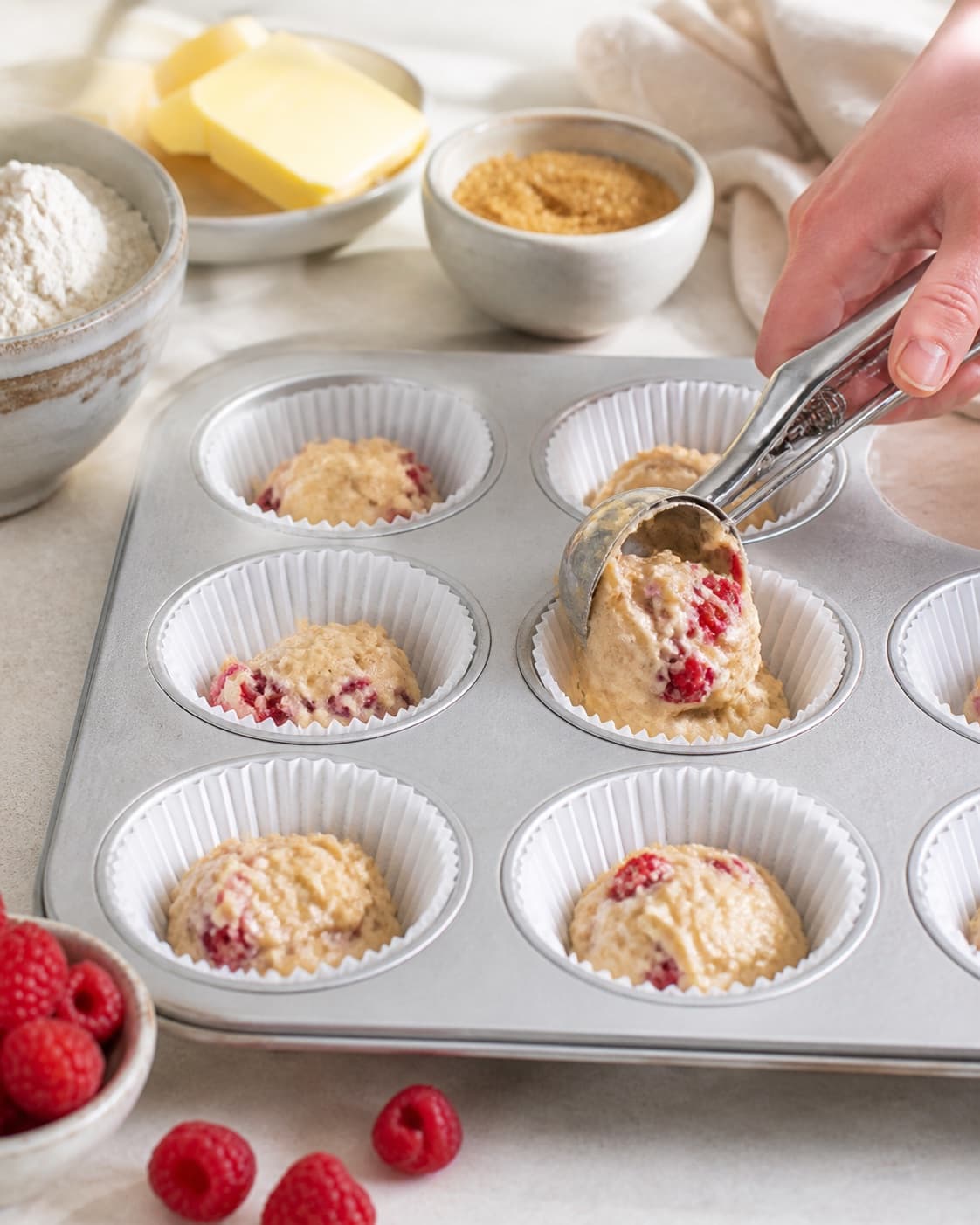 Whole raspberries being folded gently into thick batter before equal muffin portions are scooped under tilberedningen af hindbærmuffins