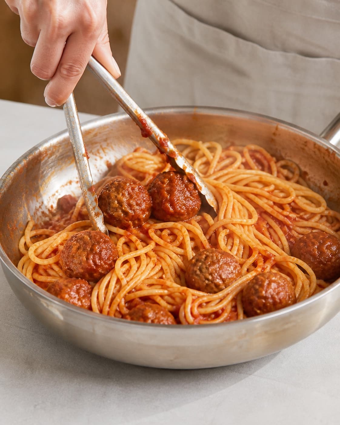 Spaghetti being tossed with tomato sauce and fully cooked beef meatballs in a broad pan under tilberedningen af spaghetti à la lady og vagabonden