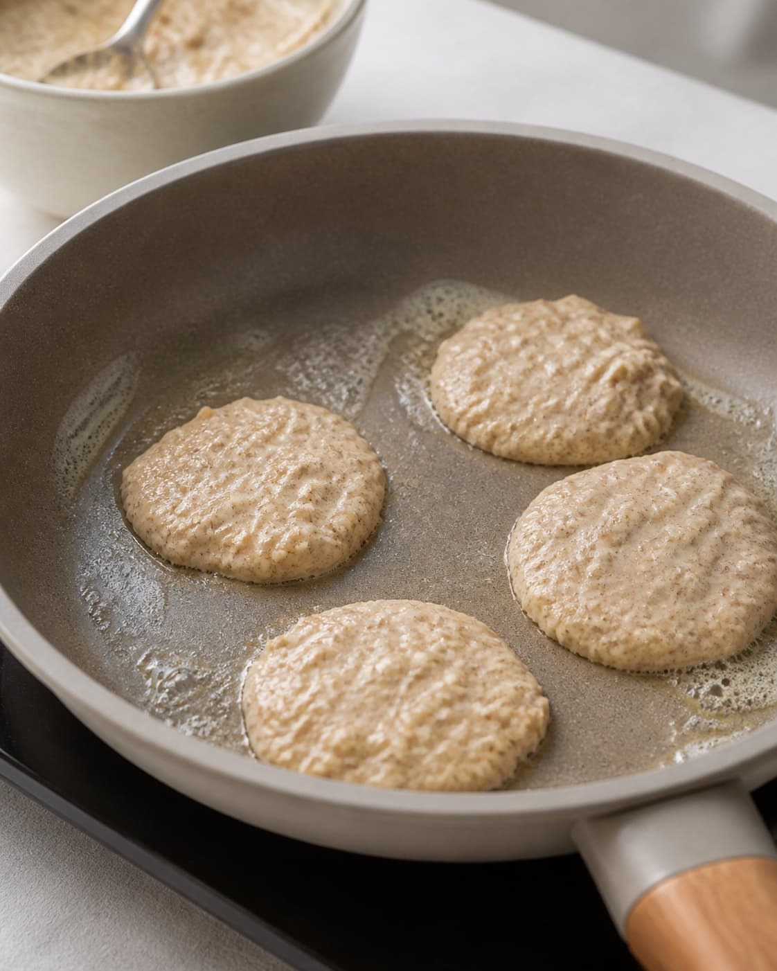 Equal spoonfuls of apple cinnamon pancake batter portioned onto a buttered pan under tilberedningen af æblepandekager med kanel