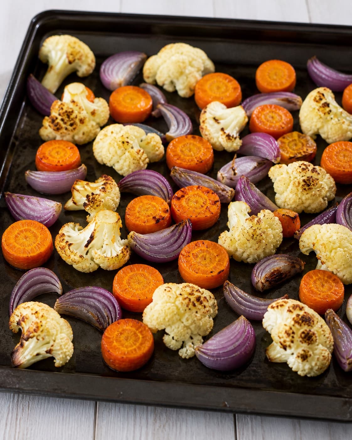 Carrots cauliflower and red onion beginning to brown on a spacious hot roasting tray under tilberedningen af grøntsagsfad