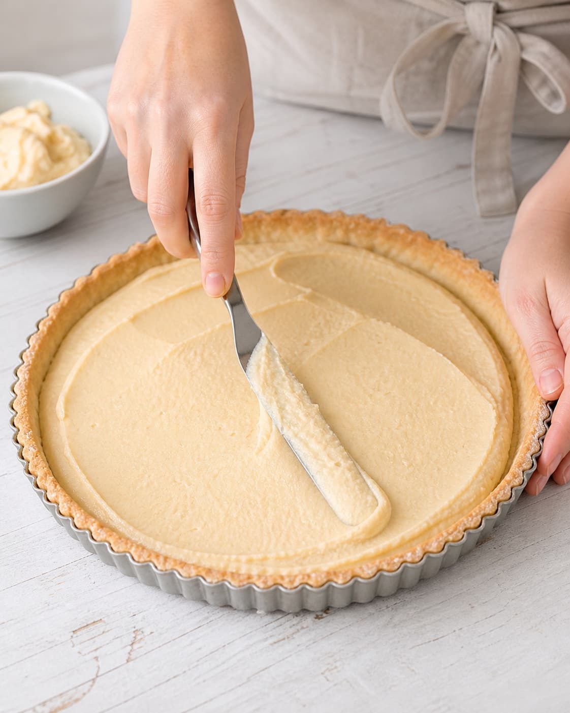 Smooth marzipan almond filling being spread evenly inside chilled pastry shell under tilberedningen af frugttærte med marcipan og friske bær