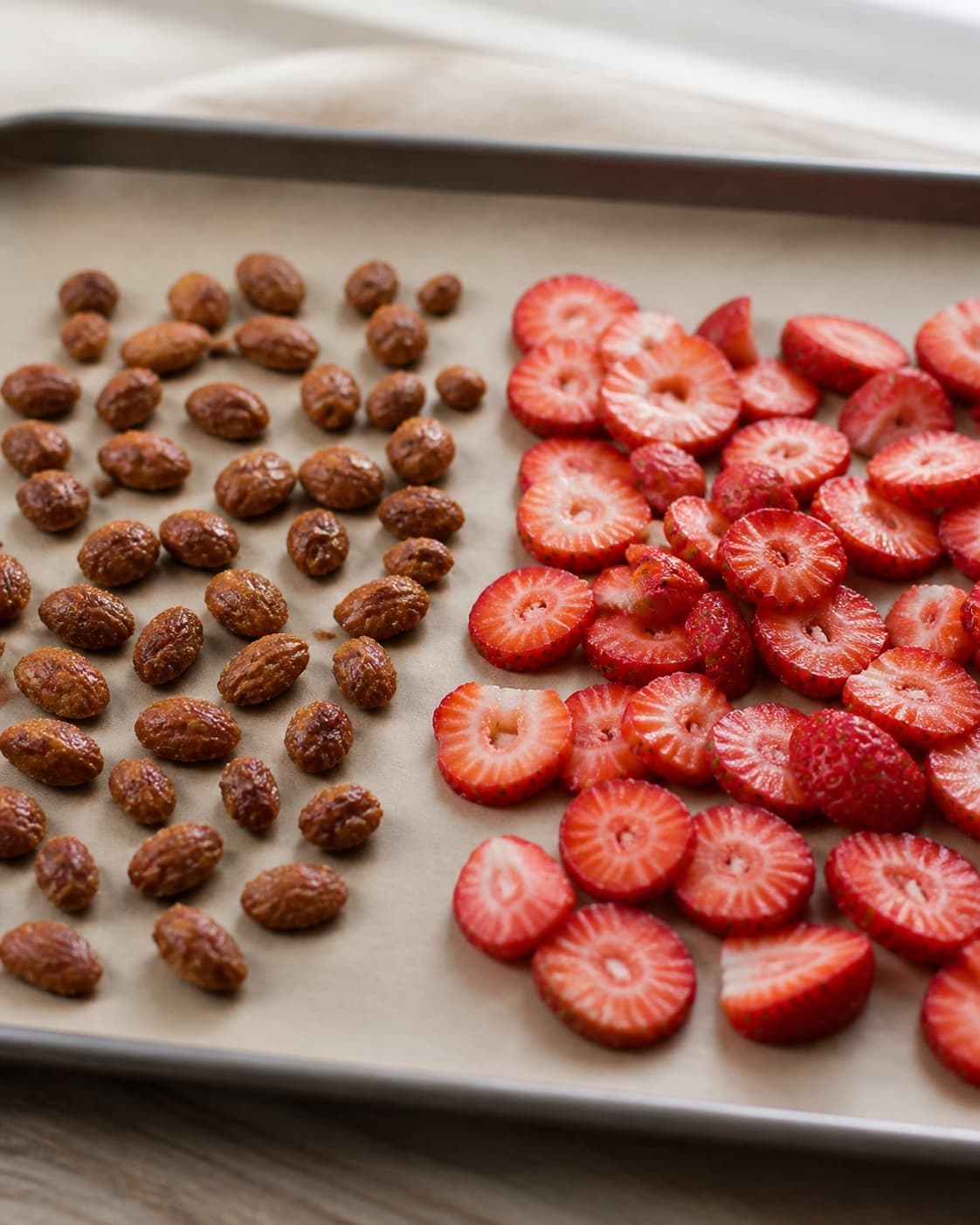 Caramelised almonds cooling in one layer beside freshly sliced strawberries under tilberedningen af koldskål med jordbær og brændte mandler