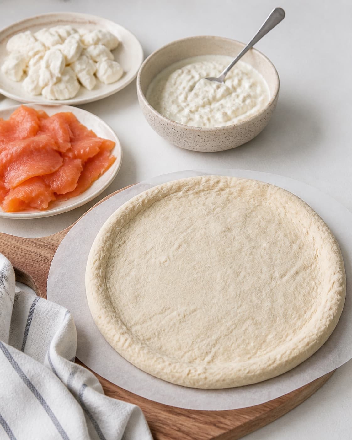 Proofed pizza dough beside drained mozzarella salmon pieces and wasabi creme fraiche under tilberedningen af pizza med laks og wasabi