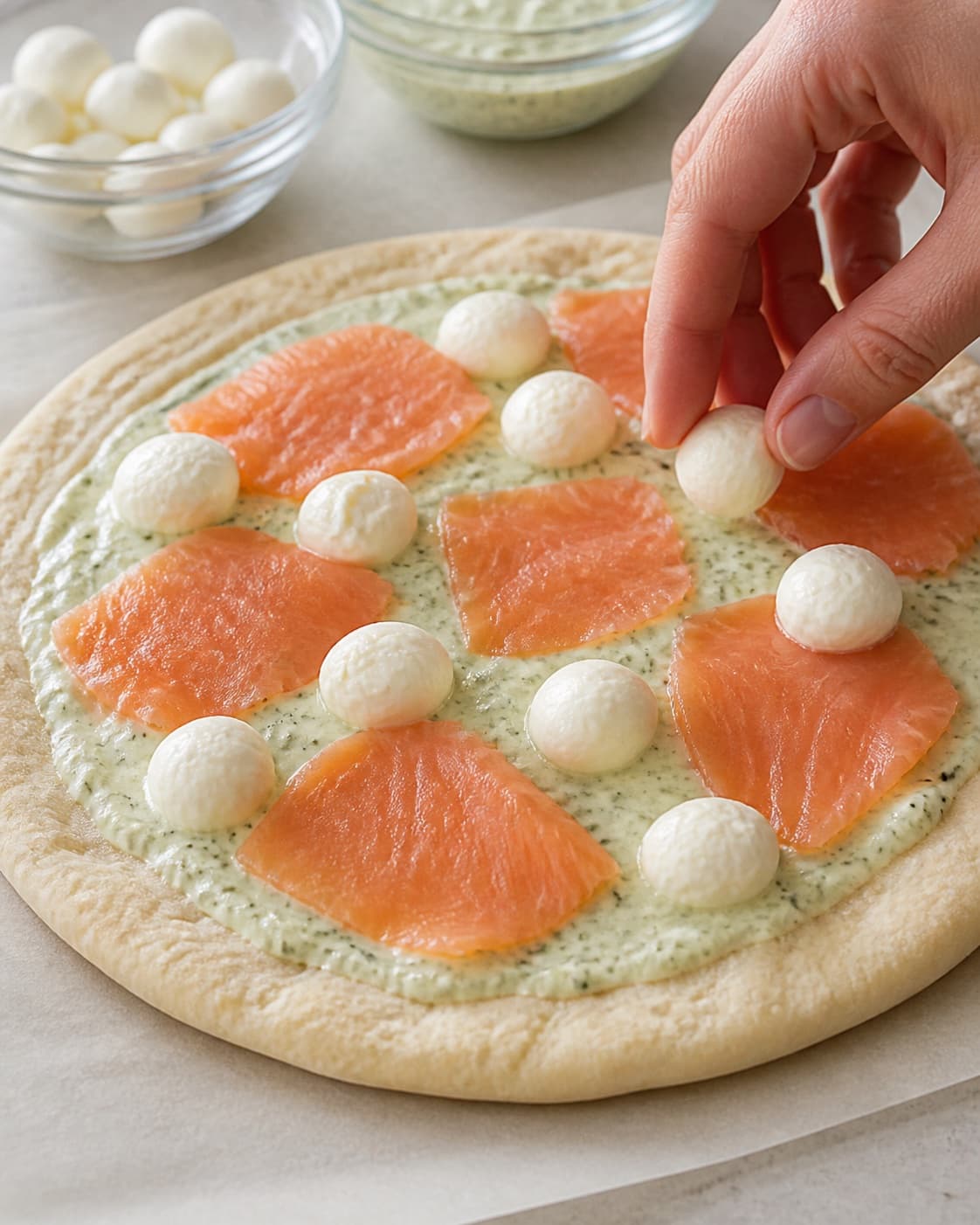Pizza dough stretched thin and topped sparingly with wasabi cream mozzarella and salmon under tilberedningen af pizza med laks og wasabi