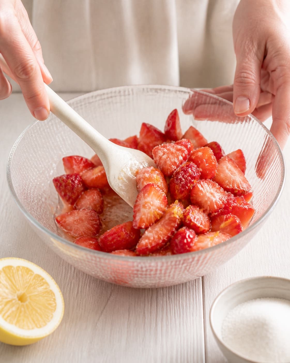 Strawberry pieces being folded with sugar vanilla lemon zest and juice under tilberedningen af jordbærdessert med mynte
