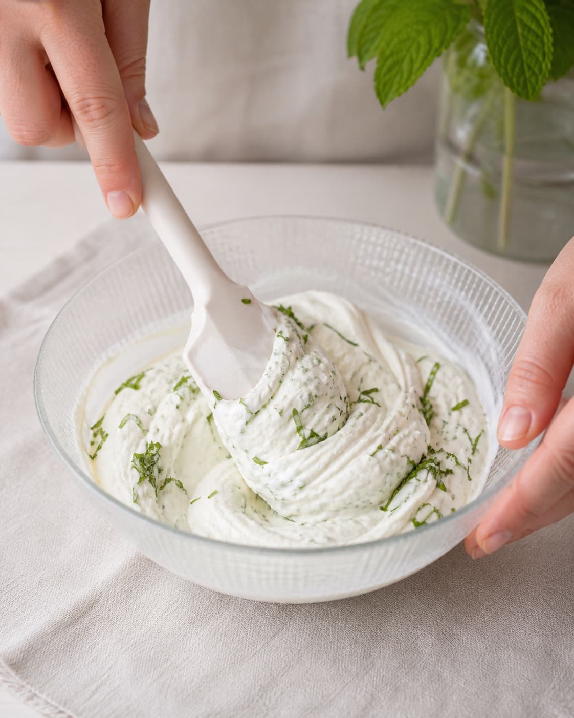 Softly whipped cream being folded into skyr with fine fresh mint ribbons under tilberedningen af jordbærdessert med mynte