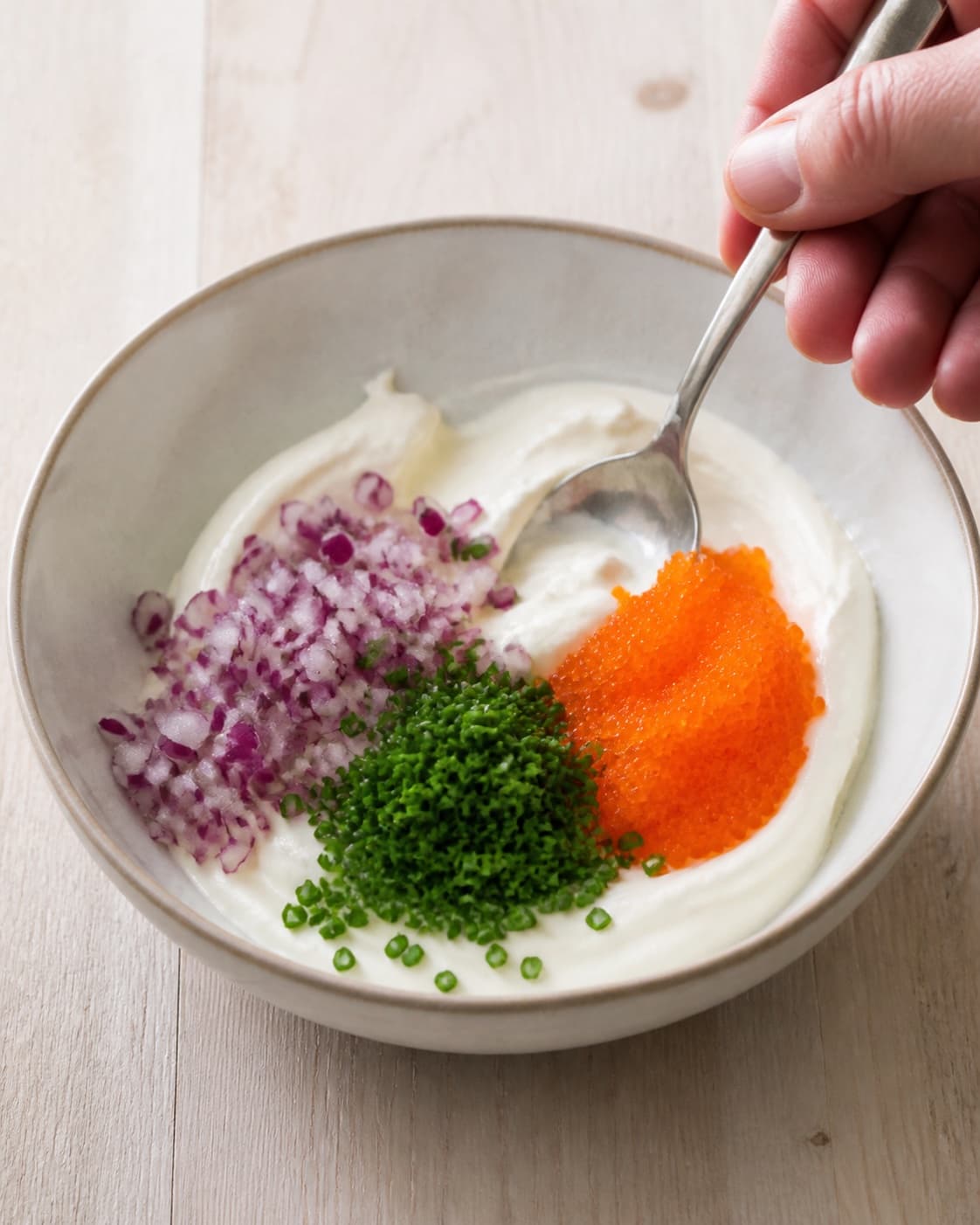 Lemon creme fraiche beside finely chopped red onion chives and chilled lumpfish roe under tilberedningen af knuste kartofler med stenbiderrogn