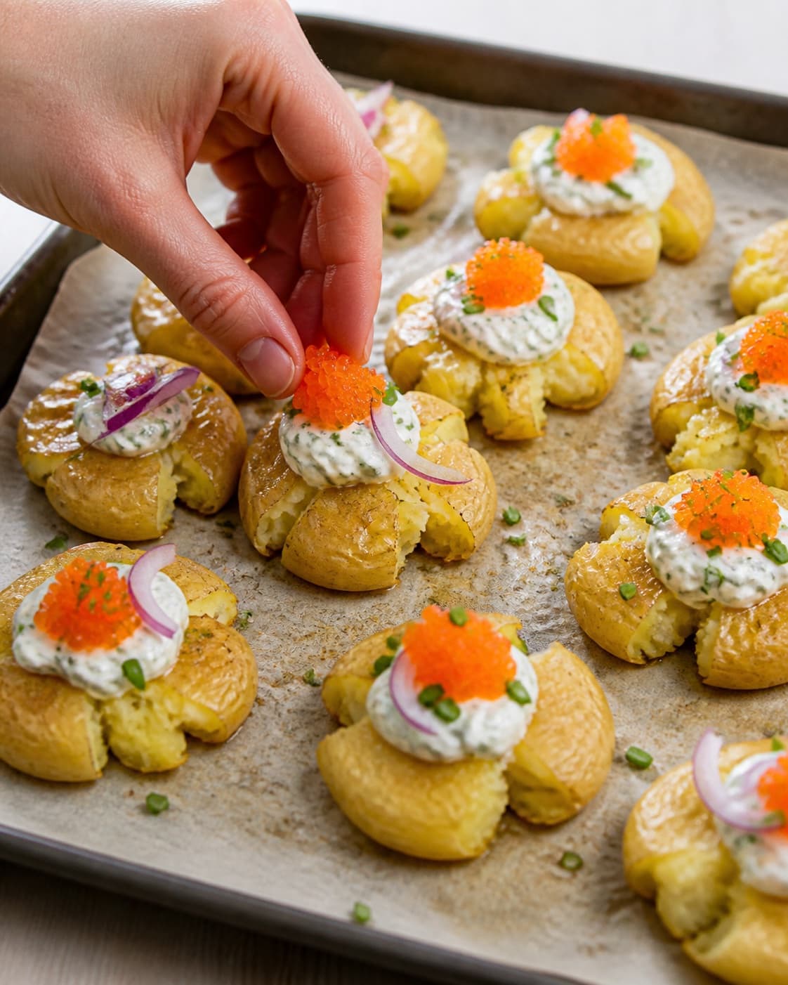 Crisp smashed potatoes topped individually with creme fraiche lumpfish roe red onion and chives under tilberedningen af knuste kartofler med stenbiderrogn
