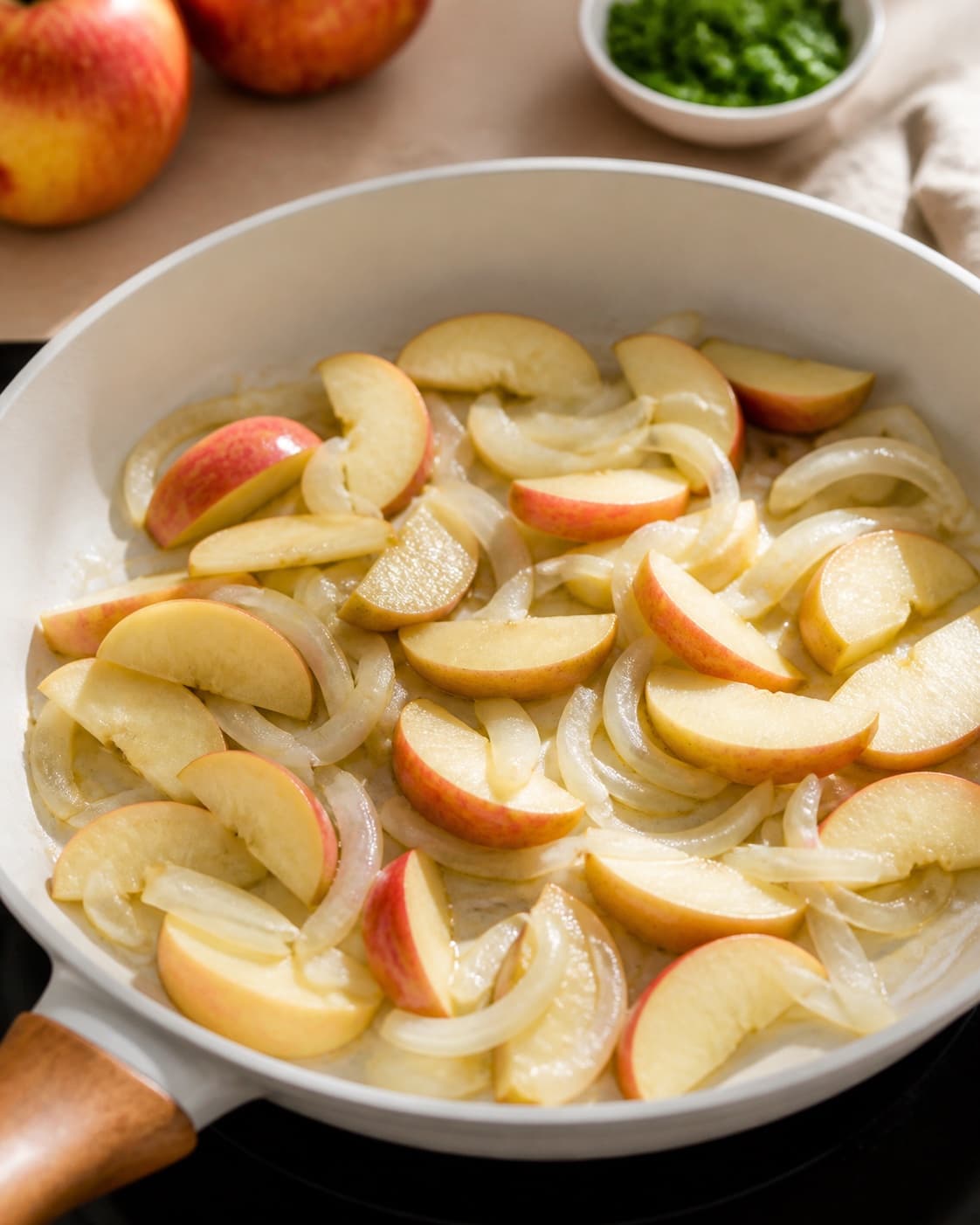 Onions and apple wedges softening with butter thyme and rendered pork fat under tilberedningen af æbleflæsk