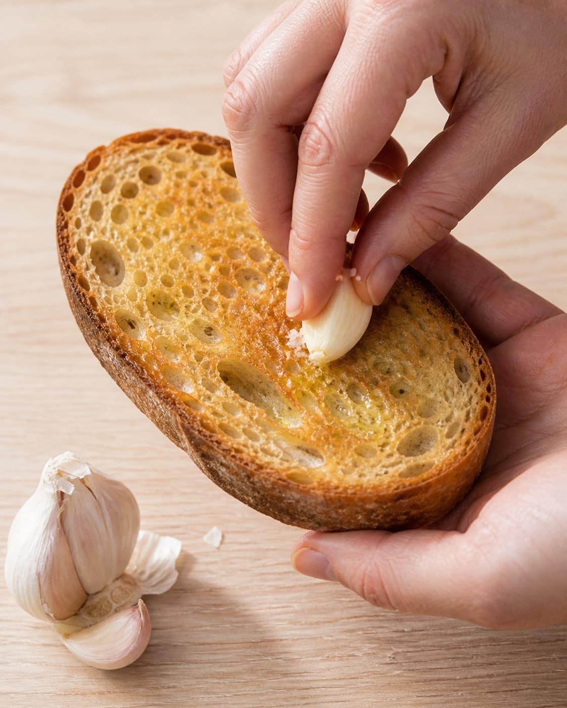 Golden sourdough toast being rubbed with garlic and lightly buttered under tilberedningen af æg med serranoskinke og tomat