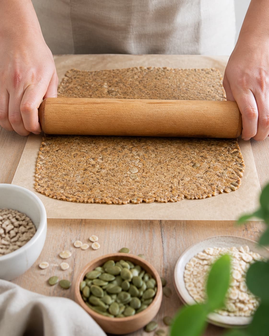 Hydrated seed dough being rolled into one uniform two millimetre sheet between baking paper under tilberedningen af knækbrød