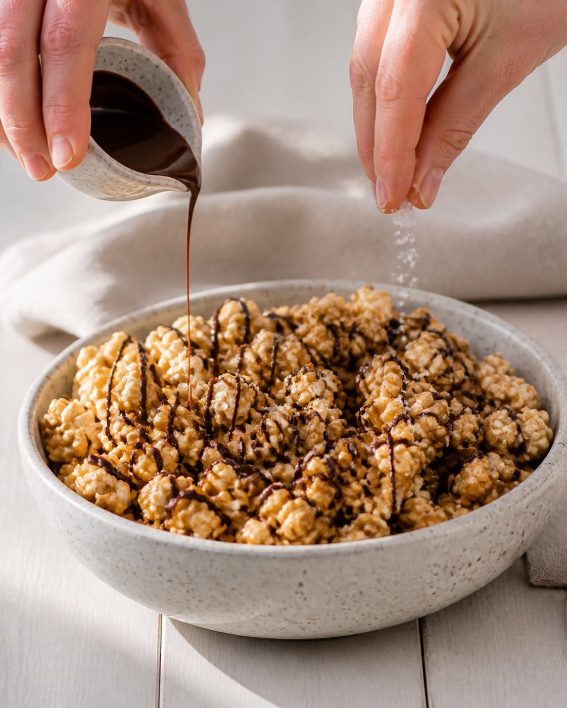 Crisp caramel popcorn receiving thin dark chocolate ribbons and a final sea salt sprinkle under tilberedningen af chokolade og karamel popcorn