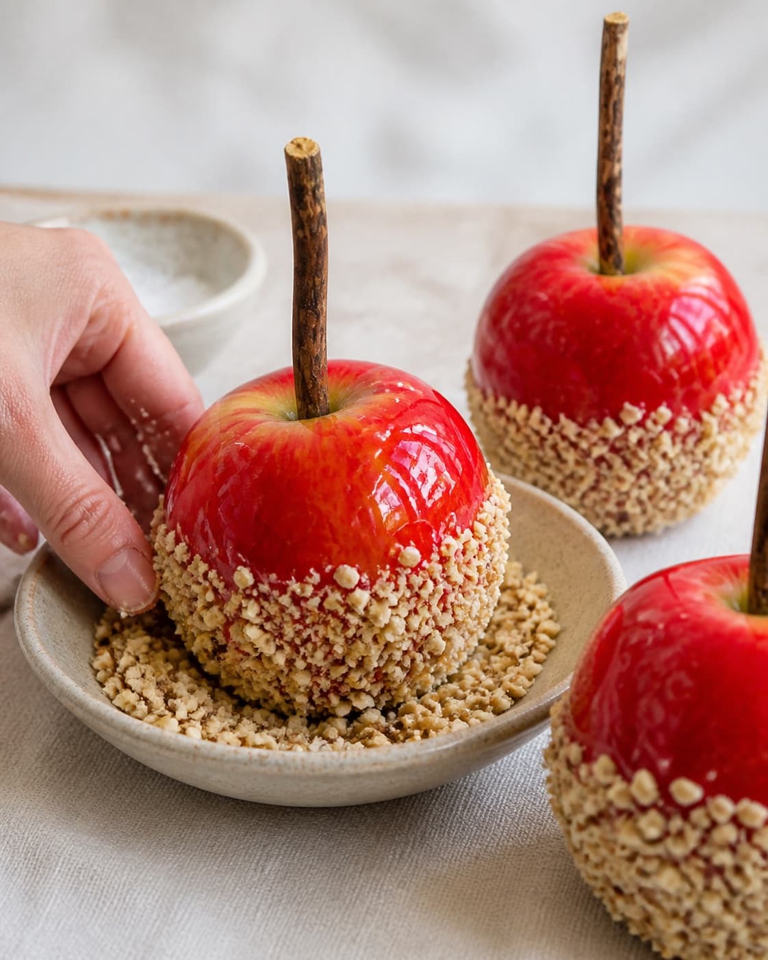 Freshly coated candy apples receiving a neat lower rim of chopped toasted hazelnuts and sea salt under tilberedningen af kandiserede æbler