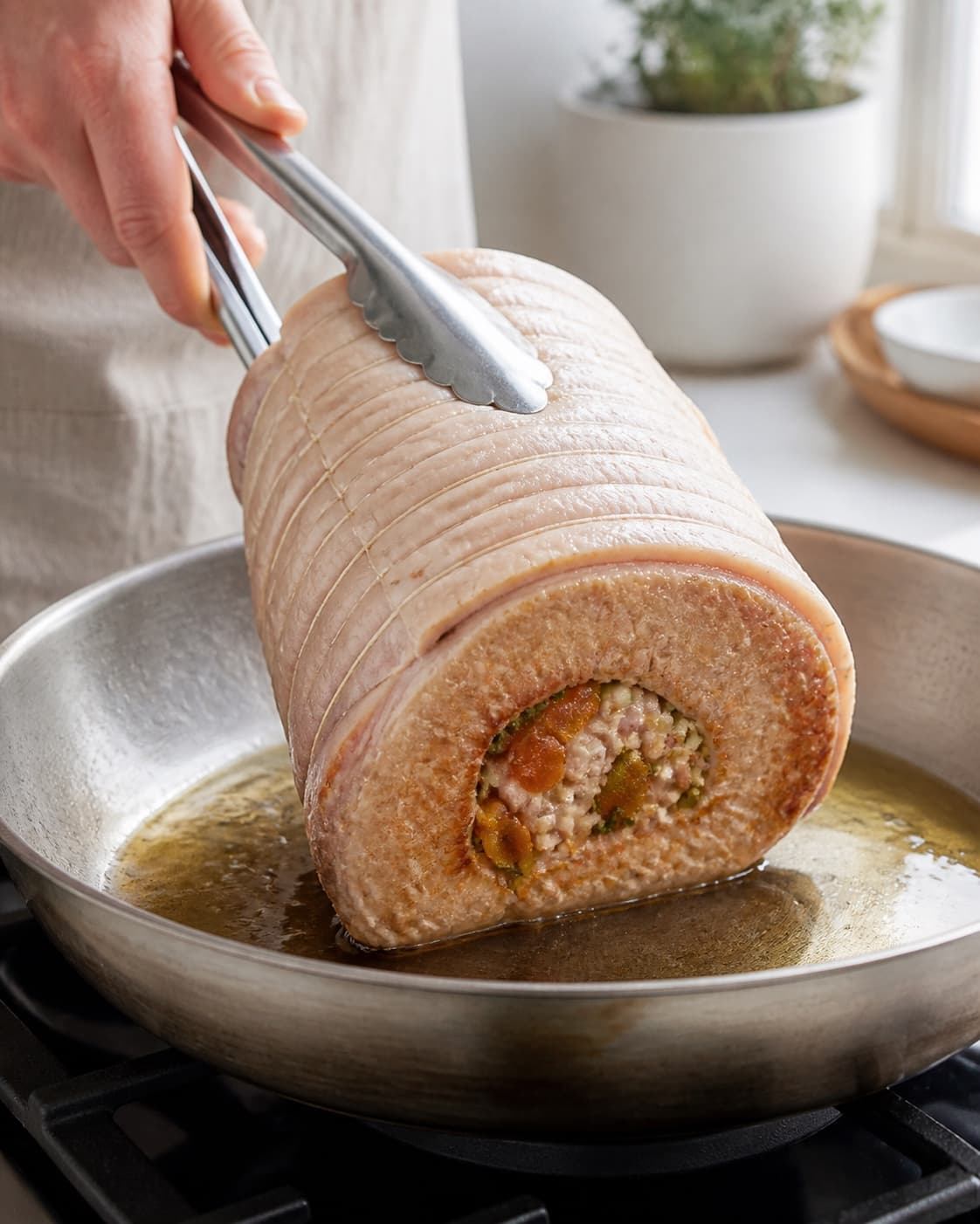 Stuffed pork roast browning on its meat sides while the scored skin stays dry under tilberedningen af flæskesteg med abrikos og timianfyld