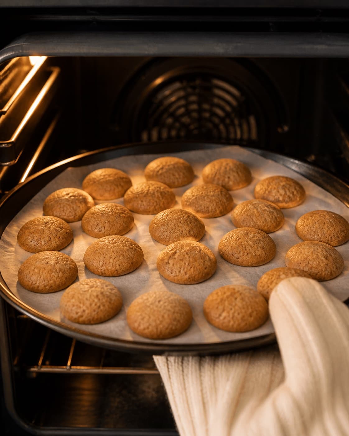 Small evenly sized peppernuts baking golden with lightly cracked set surfaces under tilberedningen af pebernødder med brun farin, ingefær og hvid peber