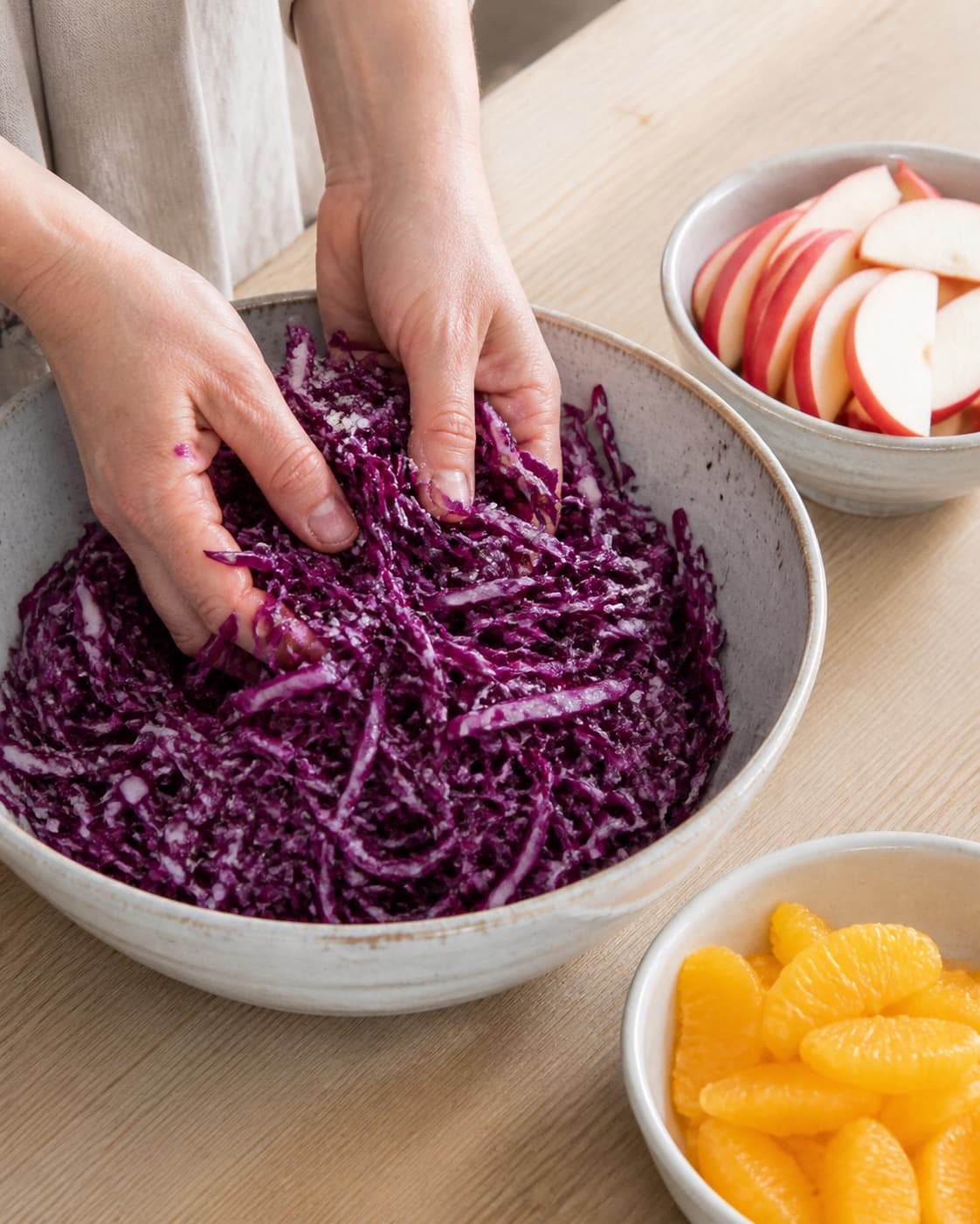 Fin red cabbage ribbons being massaged with salt while apples and orange segments remain separate under tilberedningen af vintersalat med rødkål og æbler
