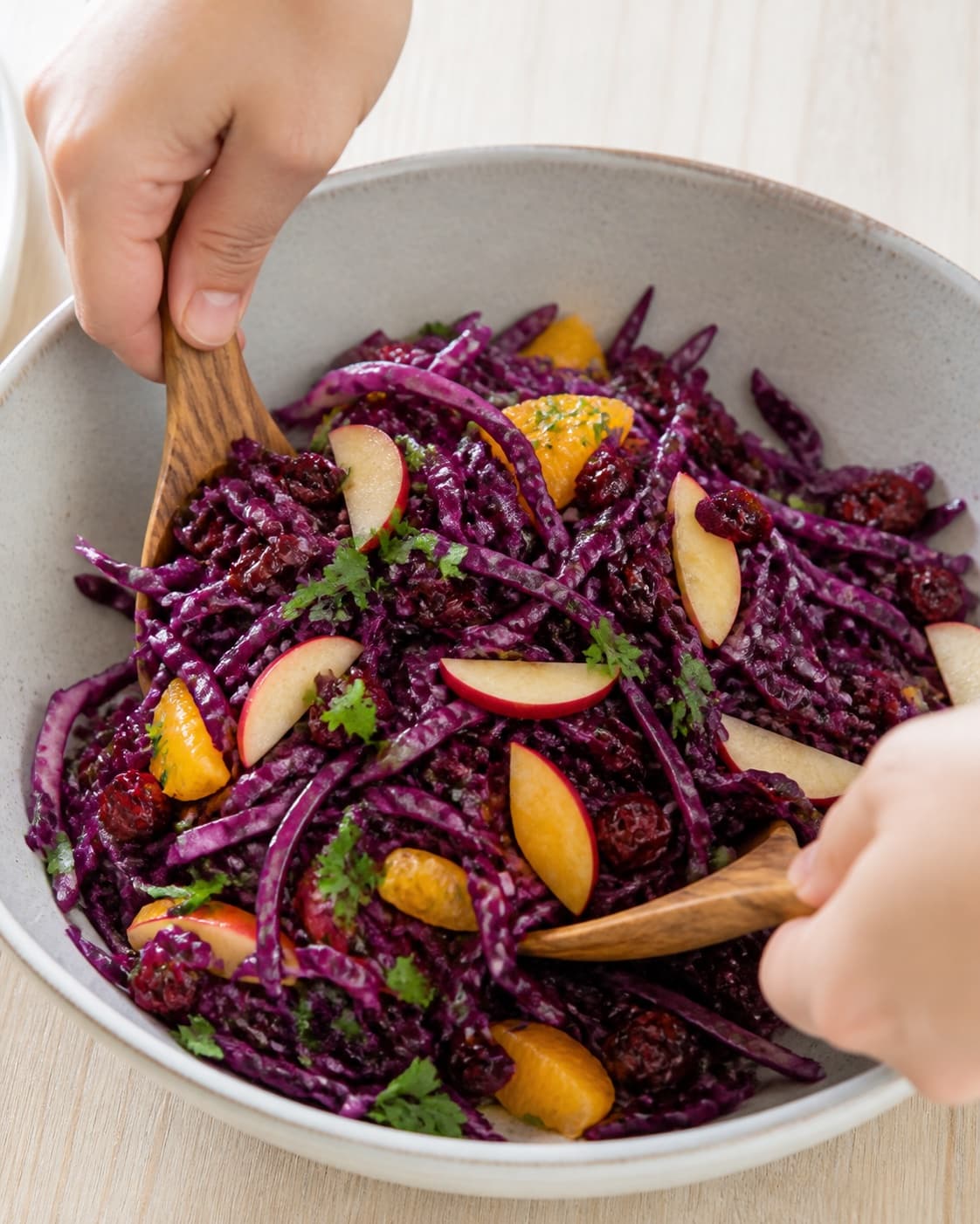 Massaged red cabbage gently combined with apple orange cranberries parsley and vinaigrette under tilberedningen af vintersalat med rødkål og æbler