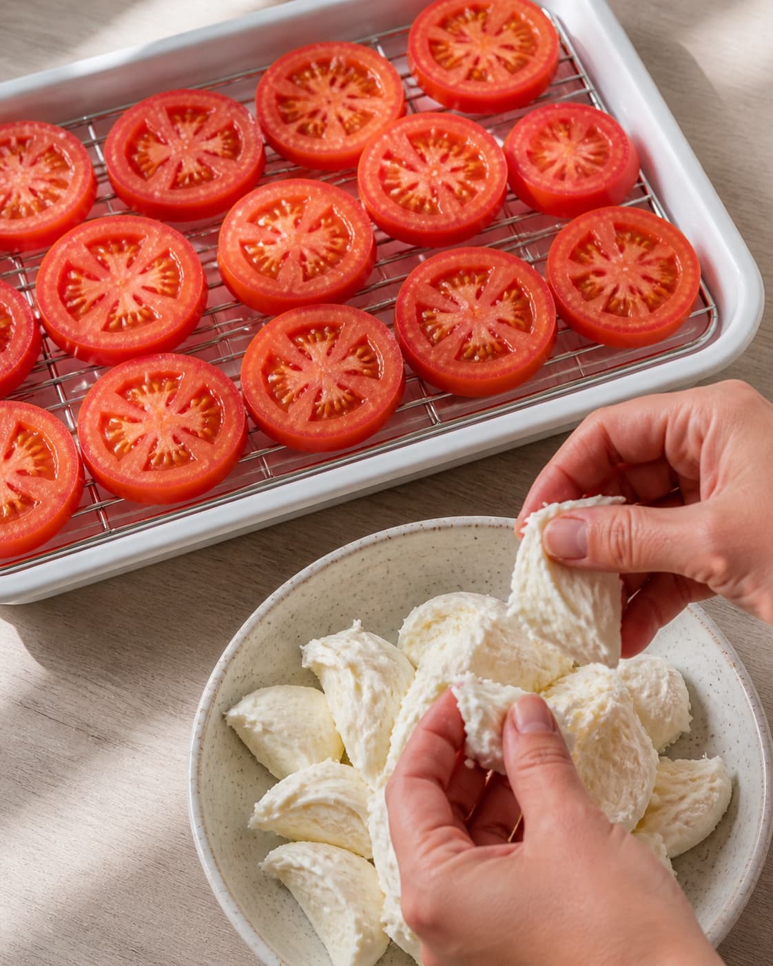 Even tomato slices lightly salted over a tray while mozzarella is torn into pieces under tilberedningen af tomatsalat med mozzarella