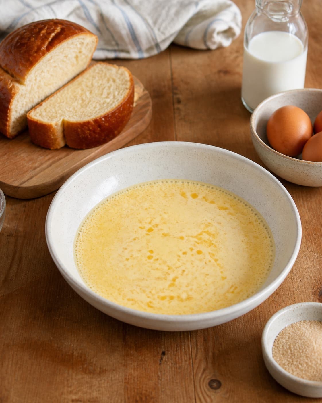 Brioche loaf beside separately measured eggs milk sugar cinnamon vanilla butter and salt under tilberedningen af arme riddere