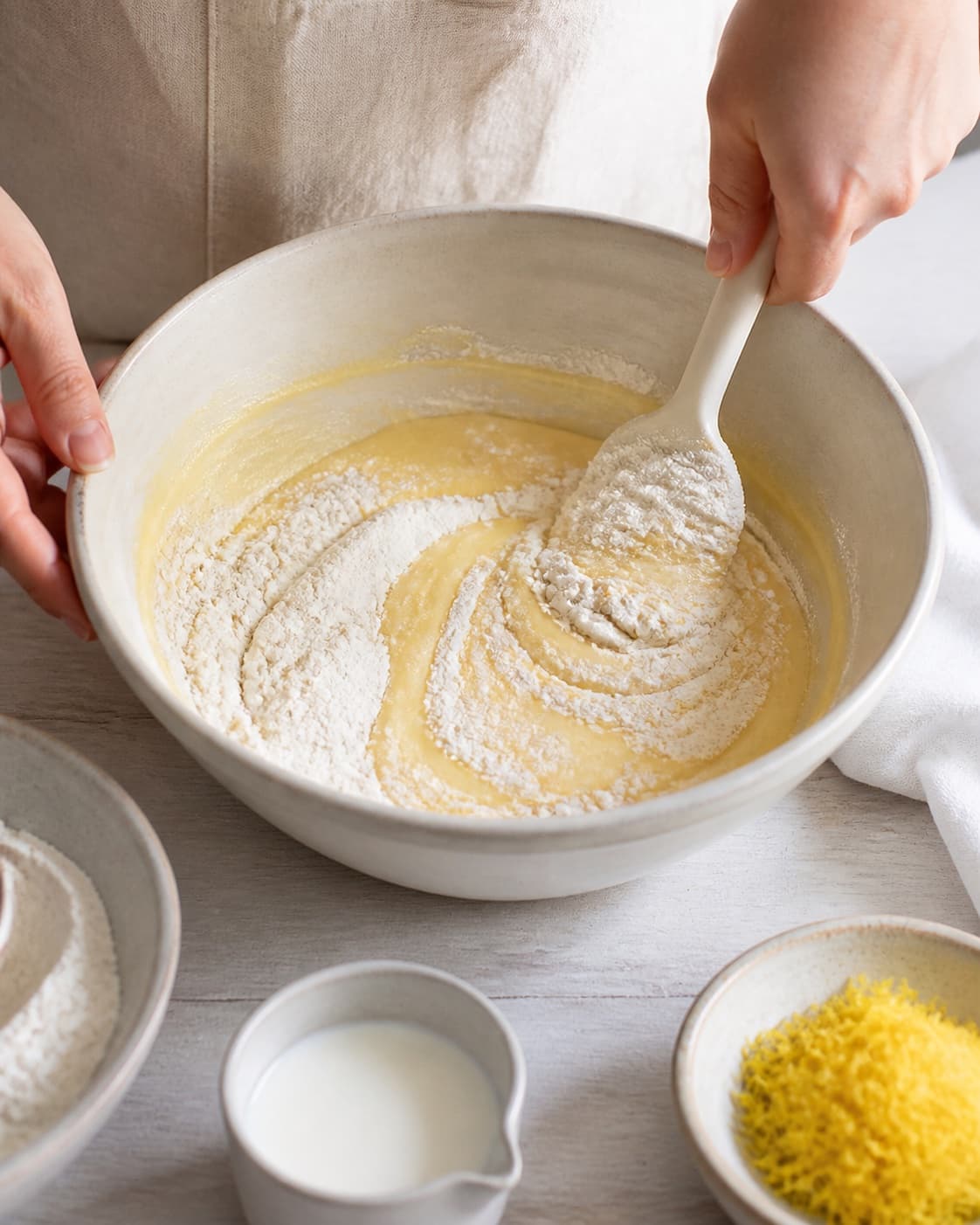 Sifted flour being folded gently into pale lemon cake batter alternating with milk under tilberedningen af saftig citronmåne med citronglasur