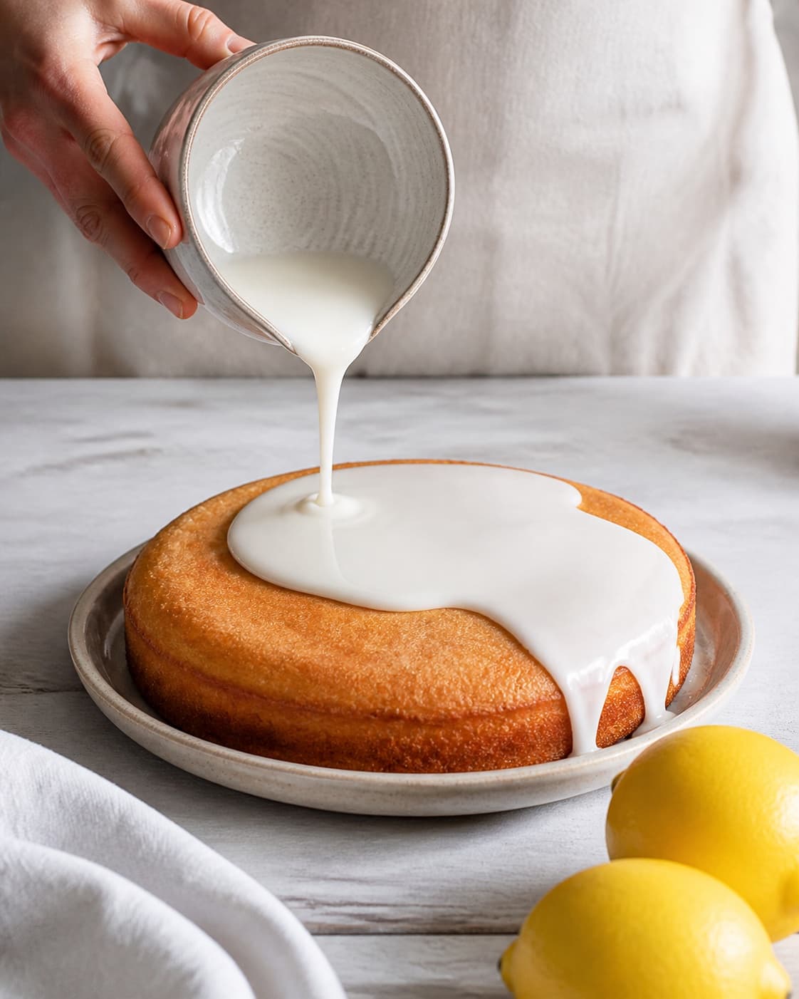 Cooled lemon cake receiving a smooth white lemon glaze after the warm cake was brushed with citrus syrup under tilberedningen af saftig citronmåne med citronglasur