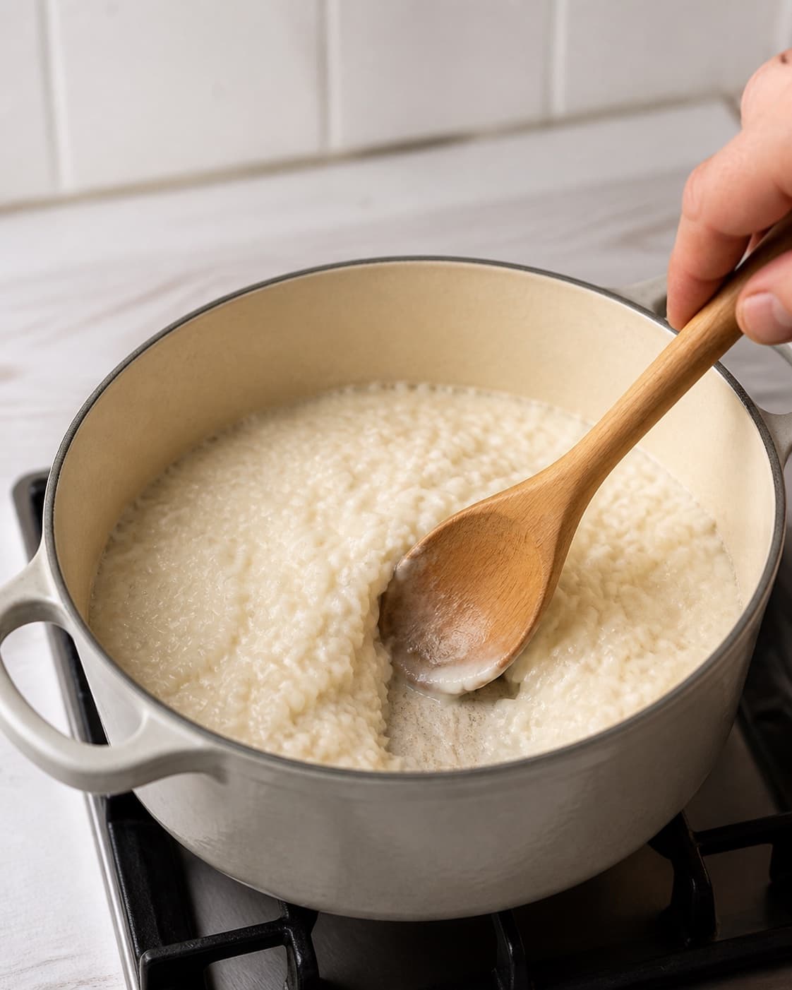 Creamy rice porridge simmering gently while a wooden spoon scrapes the pot bottom under tilberedningen af risengrød med kanel og smørklat