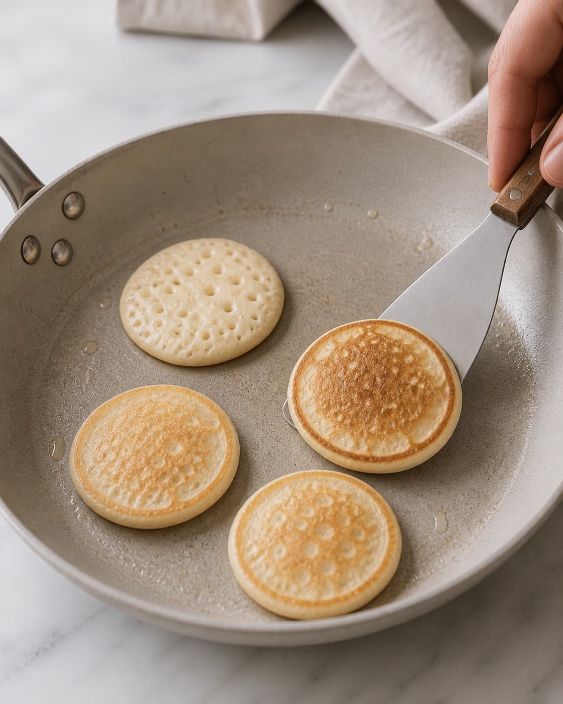 Small round blinis frying in butter and being turned after bubbles form under tilberedningen af blinis med stenbiderrogn