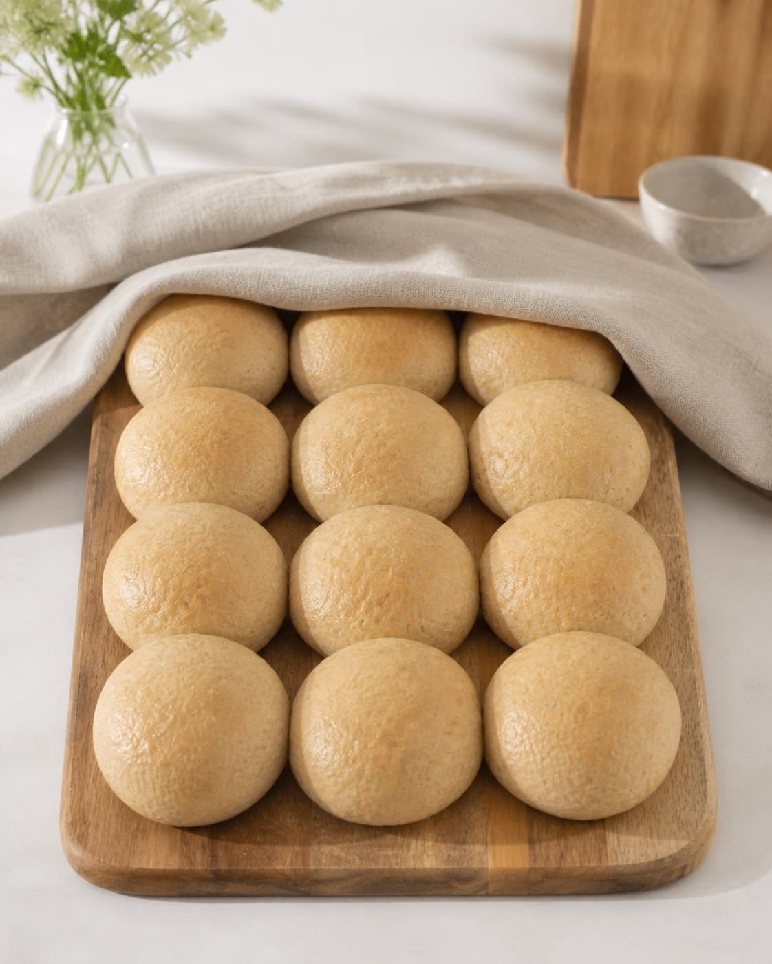 Exactly twelve lightly golden soft seedless bread rolls cooling under a clean cloth under tilberedningen af babyvenlige boller uden kerner