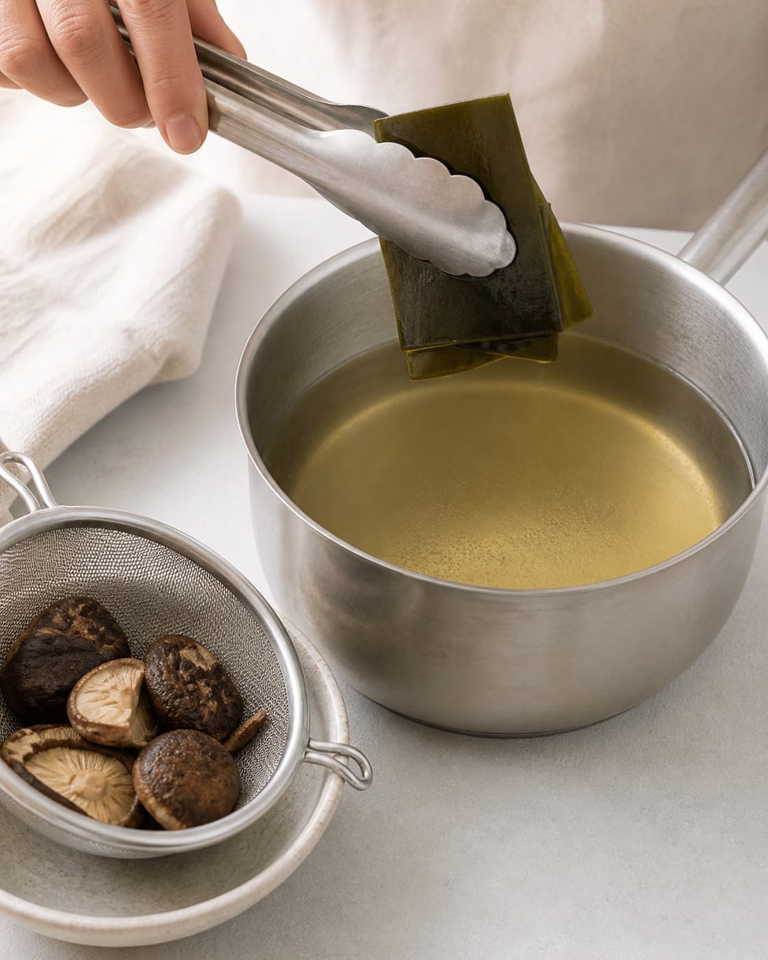Kombu being lifted from hot clear dashi before boiling and shiitake are strained under tilberedningen af misosuppe med tofu og wakame