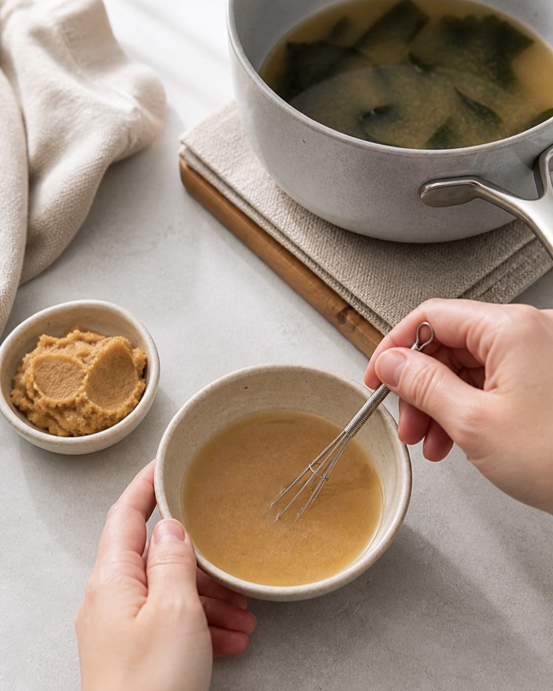 Light miso paste being dissolved in a ladle of warm broth before returning to the pot off heat under tilberedningen af misosuppe med tofu og wakame