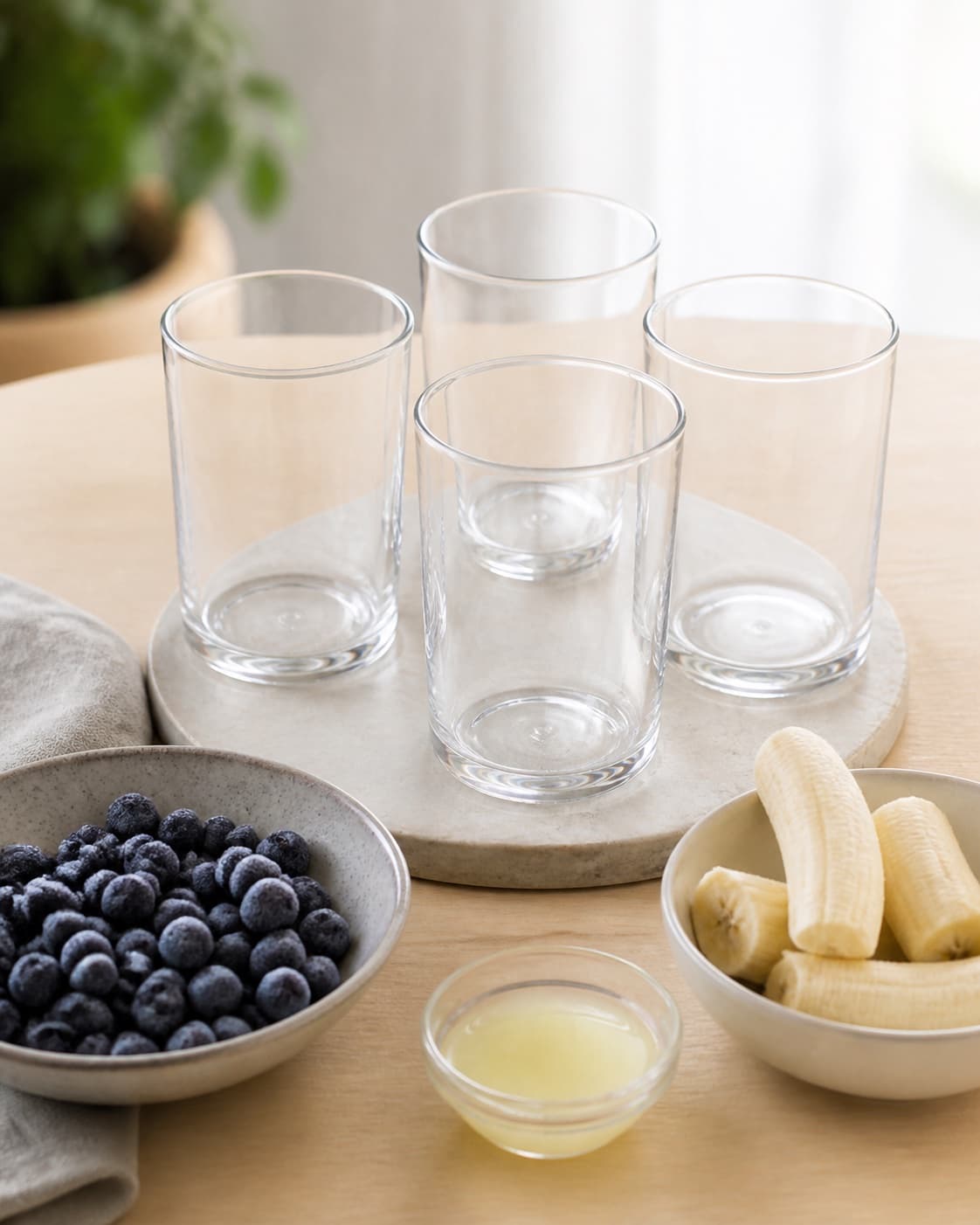 Exactly four empty chilled drinking glasses beside frozen blueberries peeled bananas and fresh lemon juice, all separate, no smoothie under tilberedningen af blåbærsmoothie