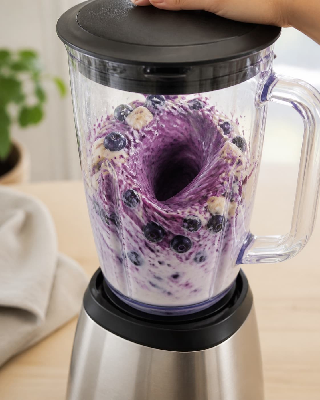 Frozen blueberries and banana actively blending into the pale yoghurt oat base, deep purple vortex, no serving glasses under tilberedningen af blåbærsmoothie